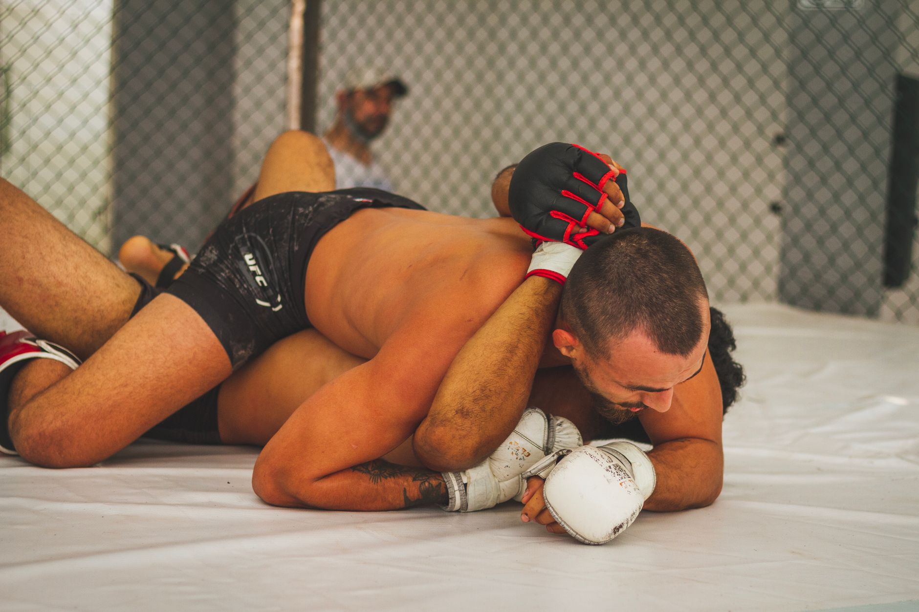Intense moment of MMA fighters grappling inside an indoor cage.