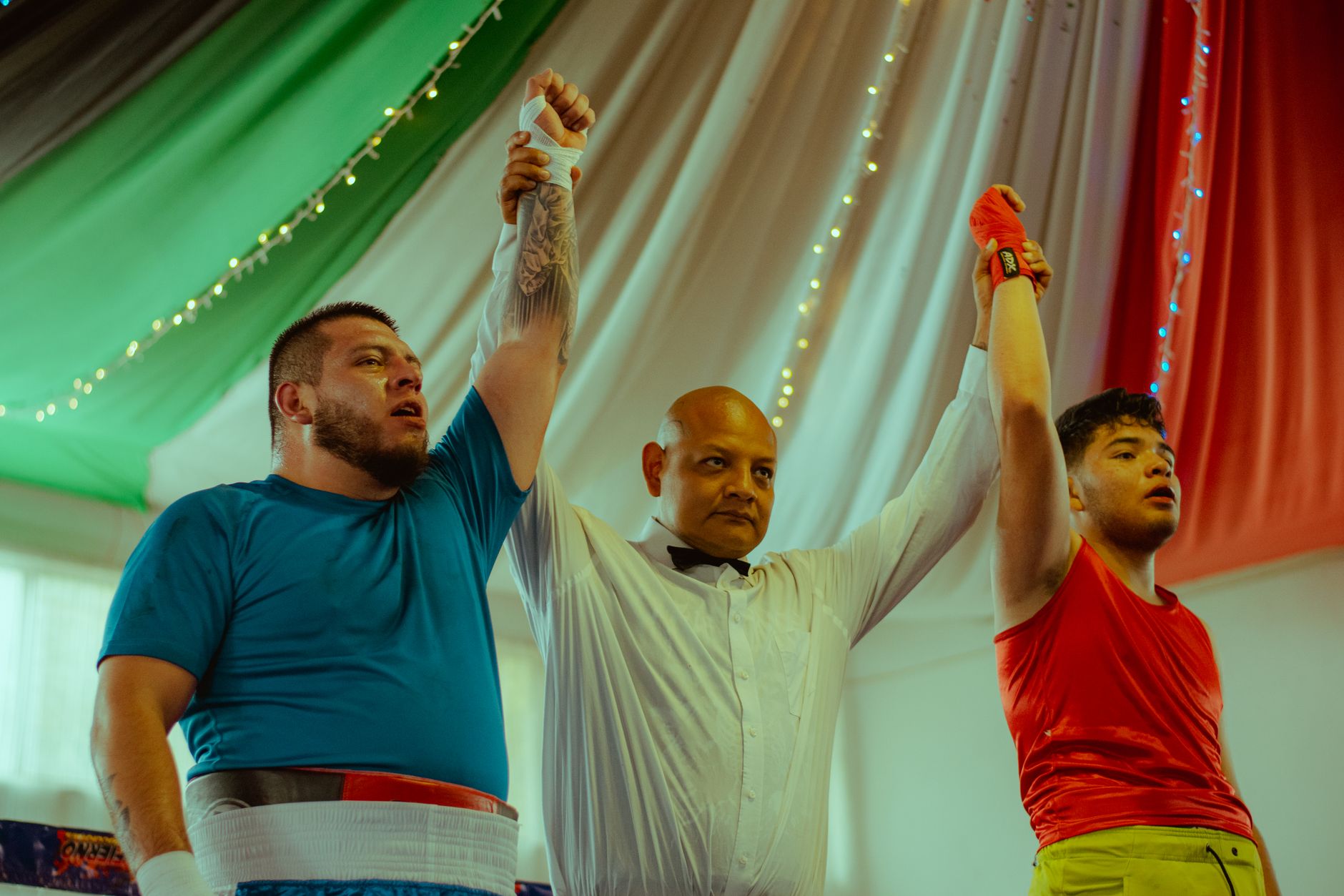 A referee declares the winner of an indoor boxing match, raising their arm in victory.