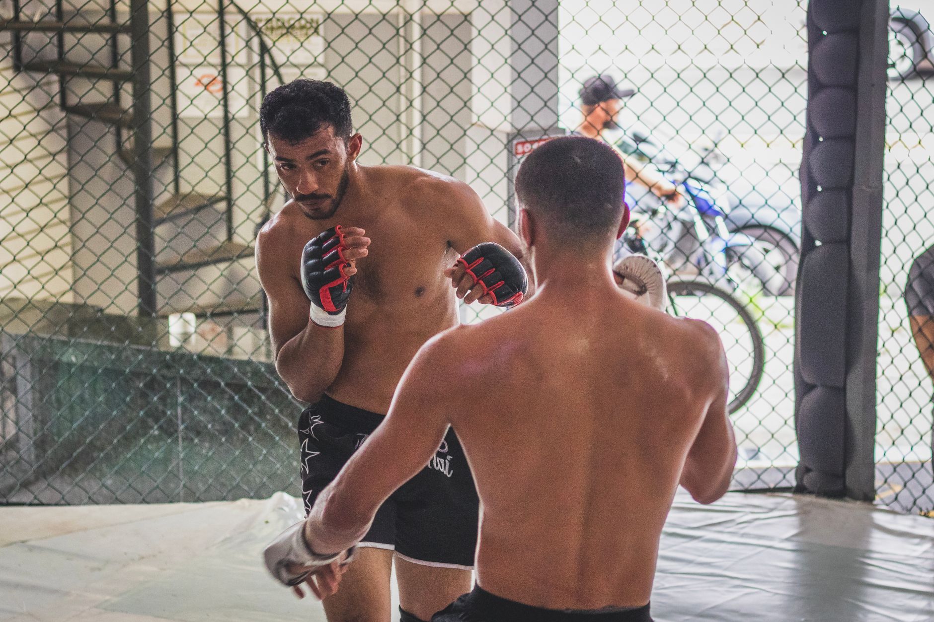 Two men engage in MMA sparring inside an octagon cage gym.