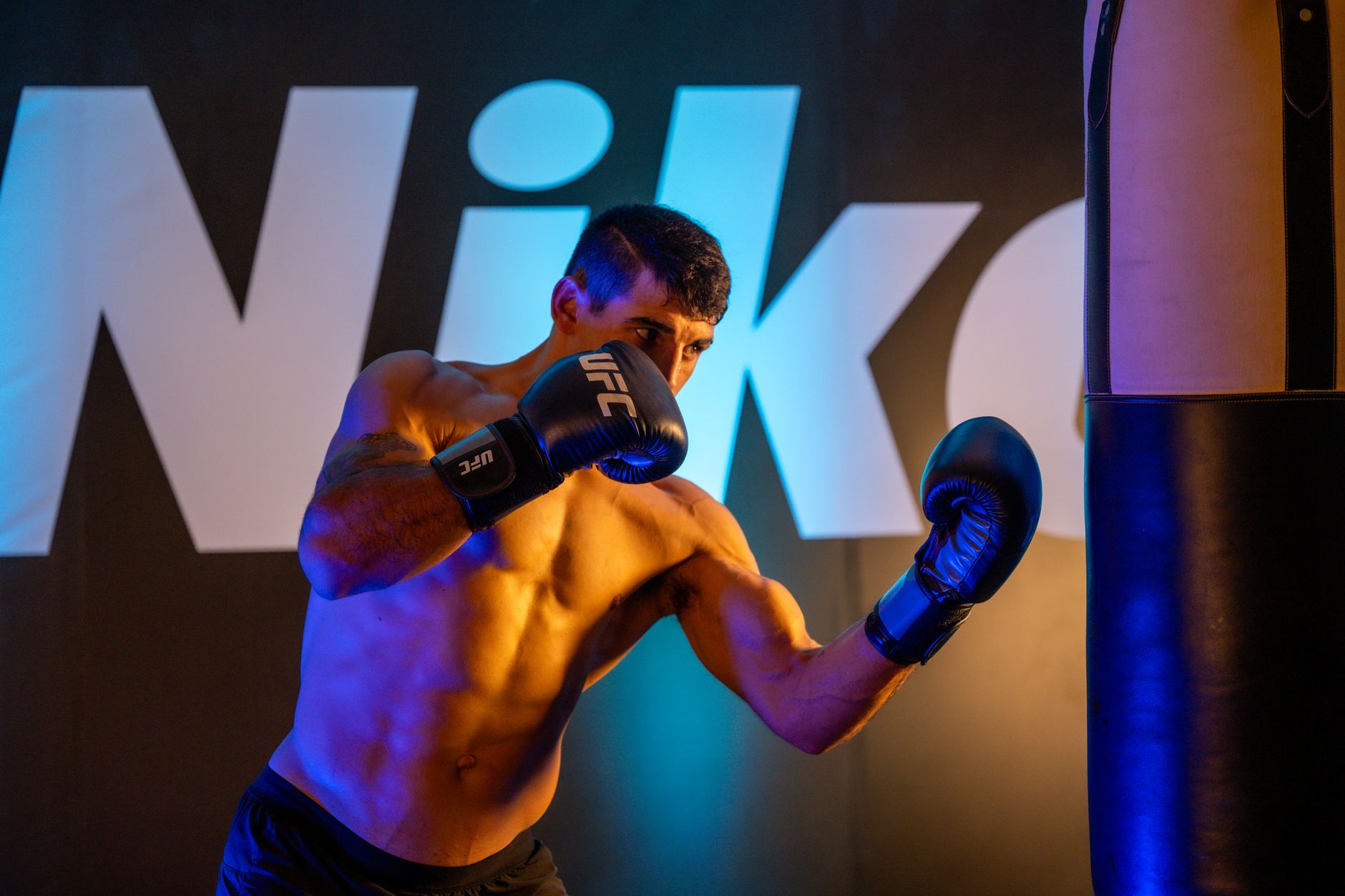 A boxer throws a punch at a heavy bag indoors, showcasing strength and focus.