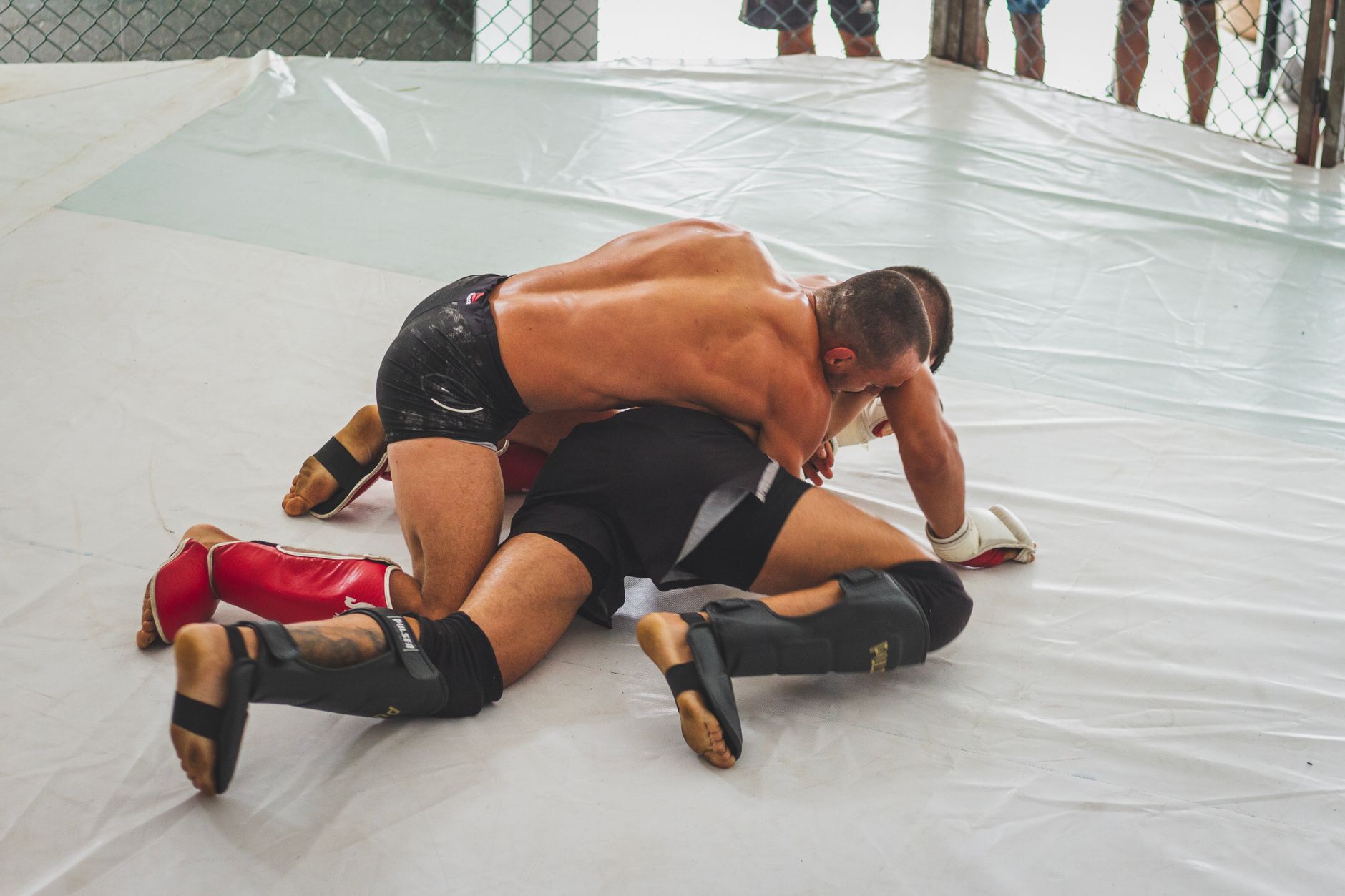 Two male MMA fighters engage in intense grappling on the mat indoors.