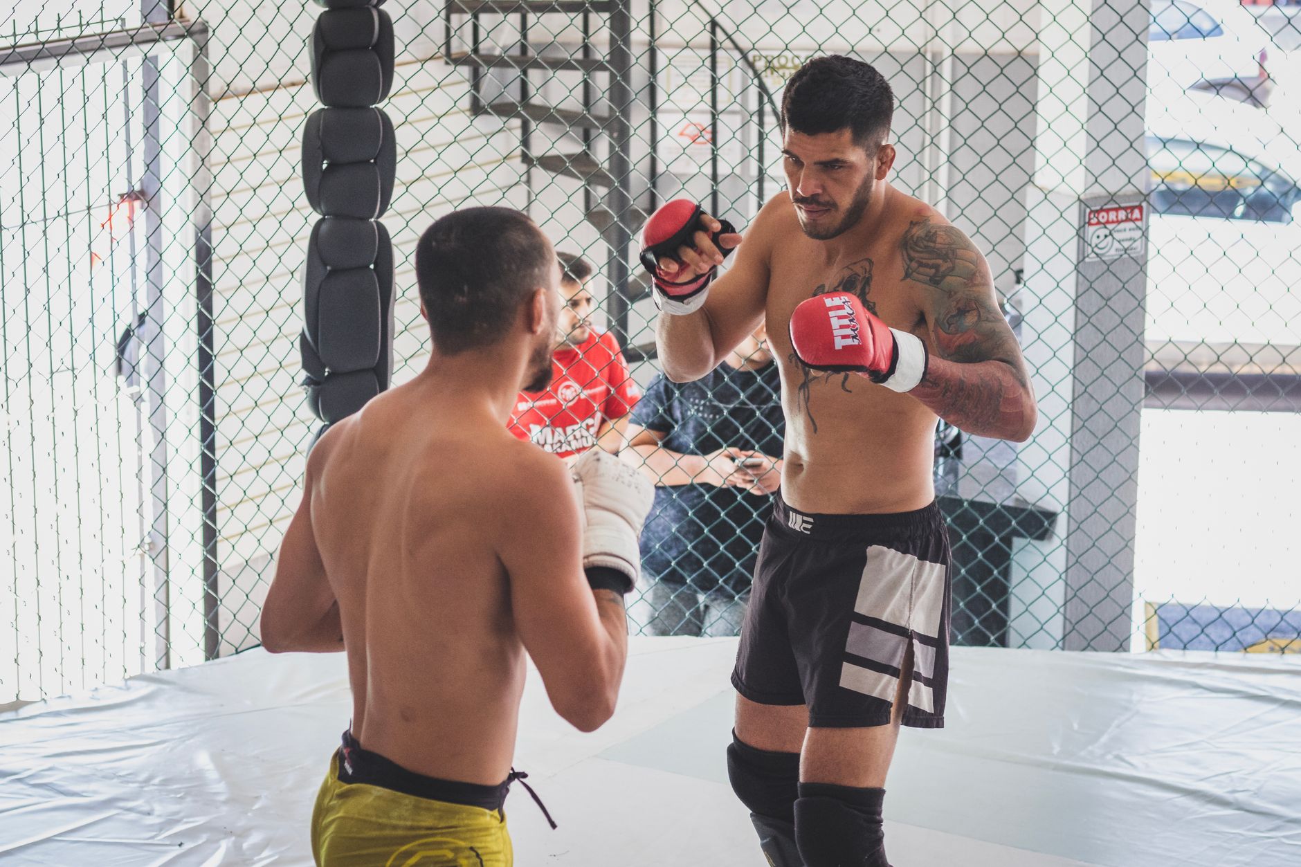 Two male fighters sparring in an indoor MMA cage gym, showcasing martial arts skills.