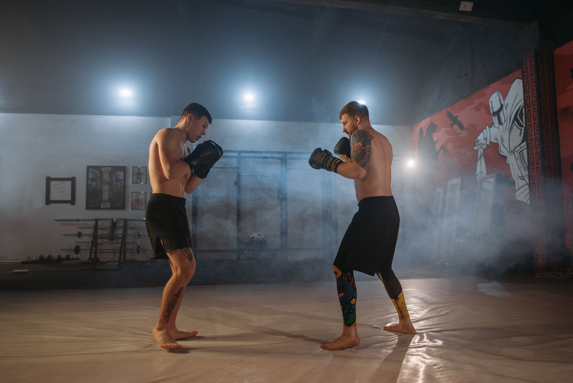 Two shirtless men sparring in a smoky gym setting, emphasizing fitness and combat skills.