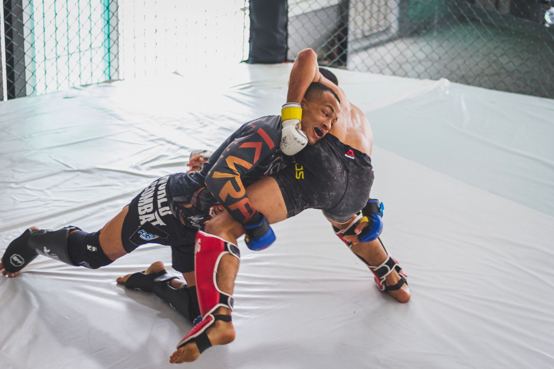 Two athletes engage in a dynamic mixed martial arts sparring match in an indoor training cage.