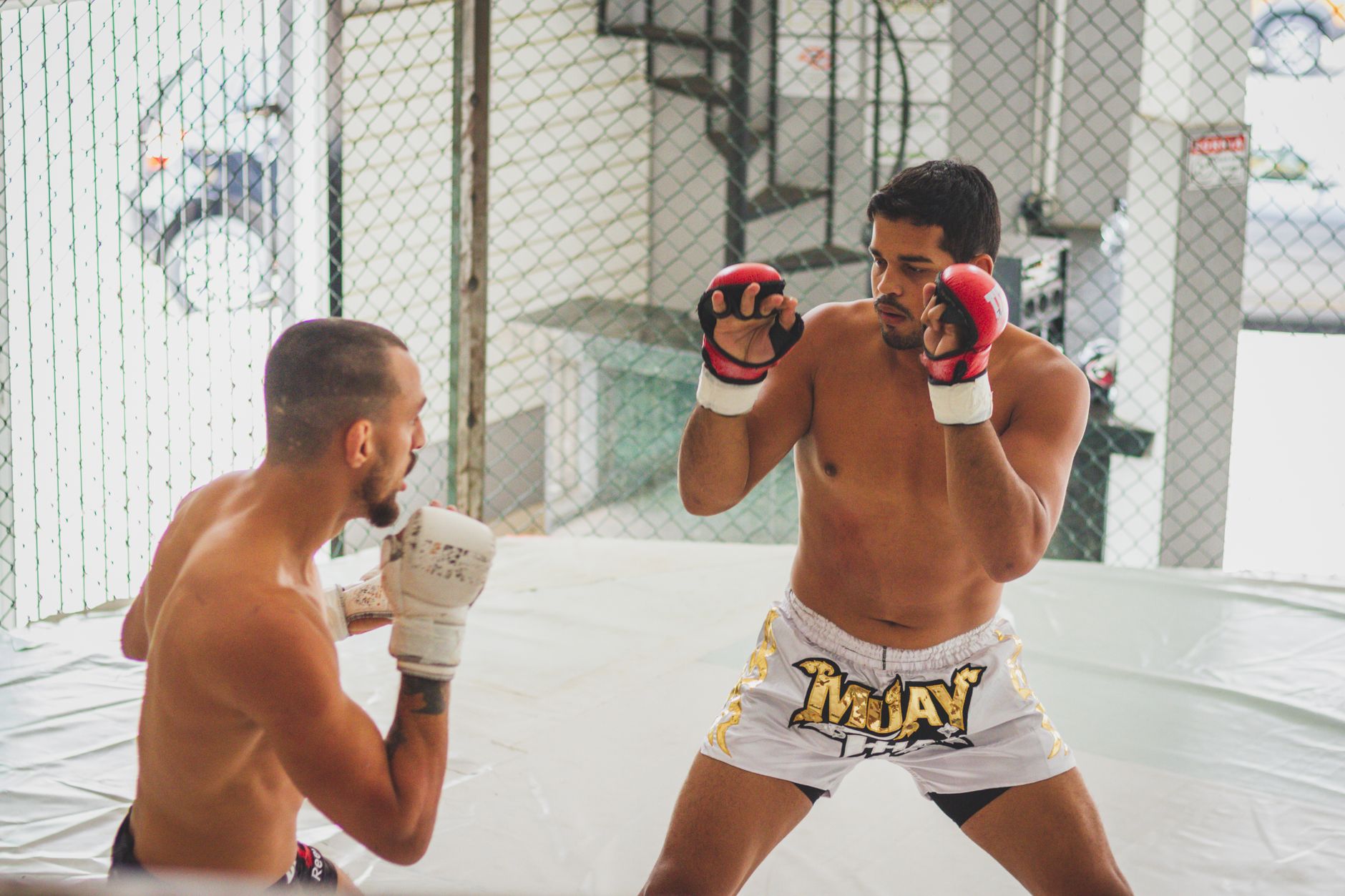 Two athletes engage in a focused Muay Thai practice session within a gym's training cage.