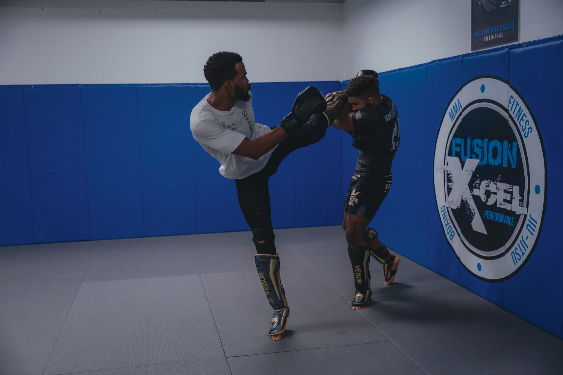 Two male MMA fighters practice a high kick in an indoor gym setting, showcasing athleticism and skill.