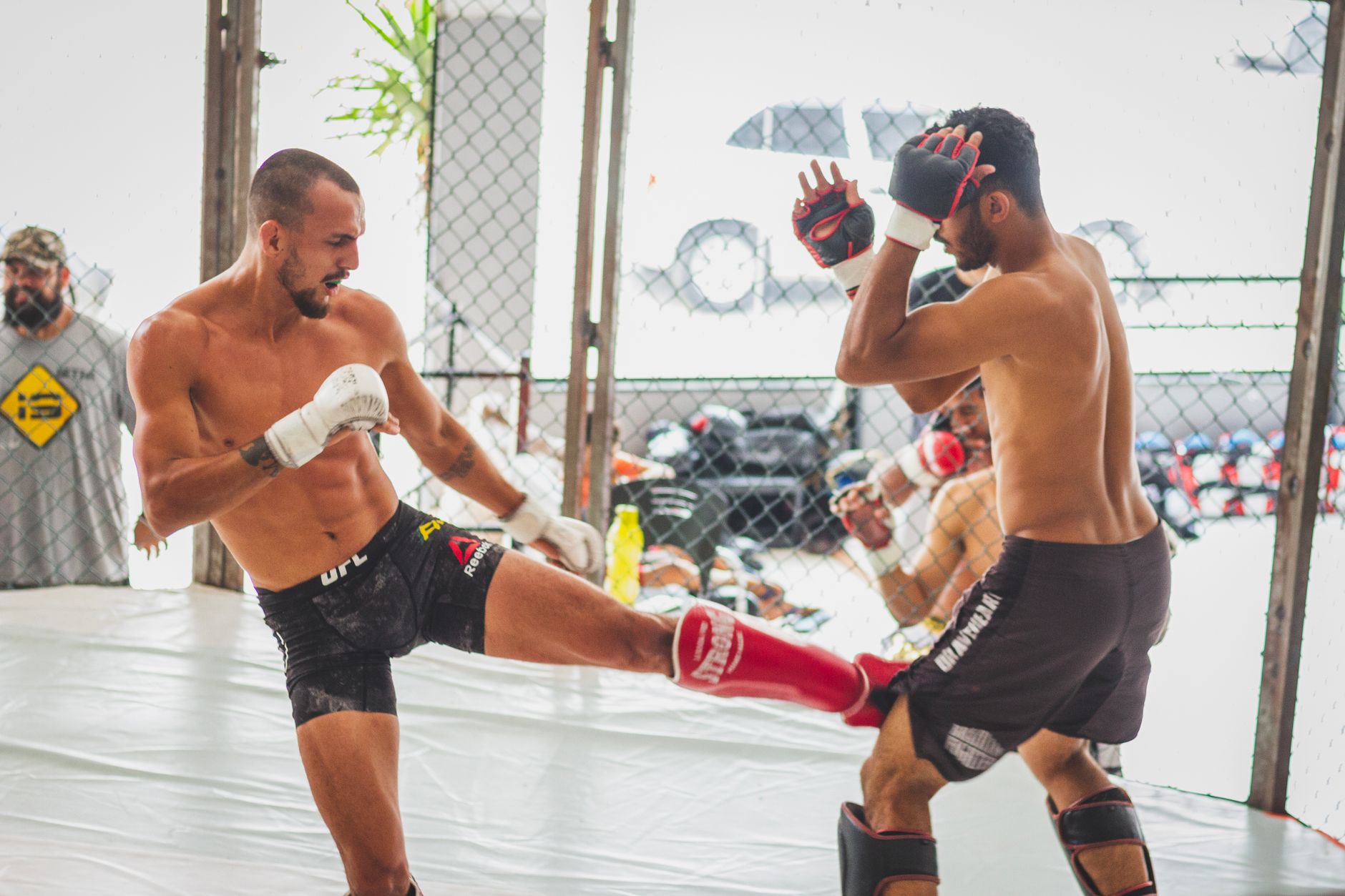 Two fighters practicing kicks and defense in a gym, showcasing martial arts skills.