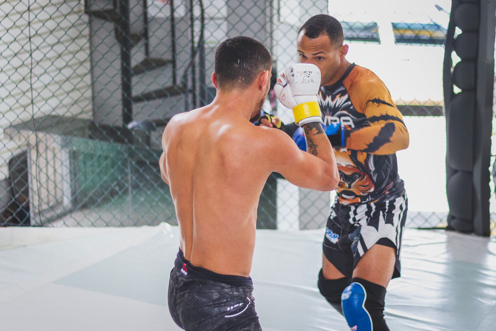 Two men engaging in martial arts sparring session indoors, showcasing intense training.