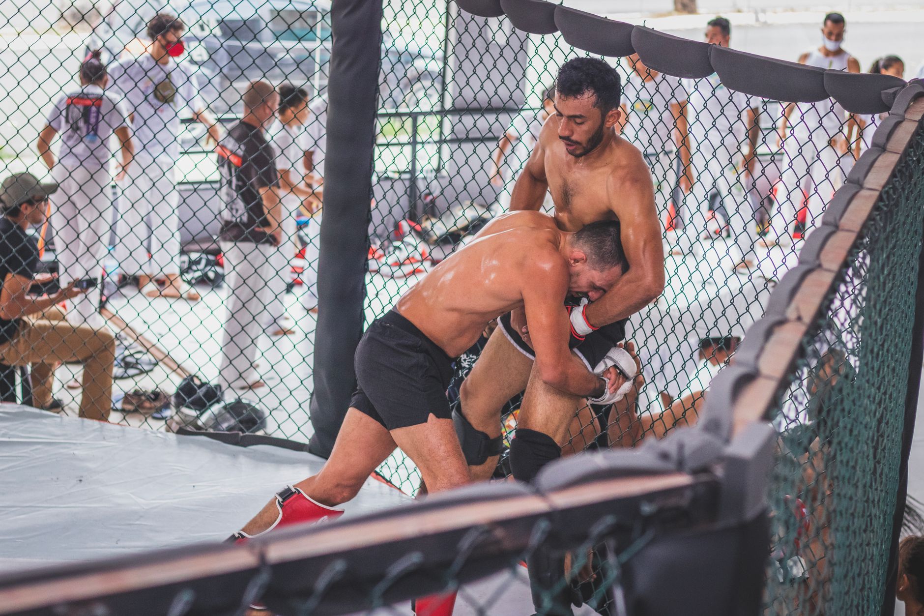 Two male MMA fighters engaging in an intense training session inside a gym cage.
