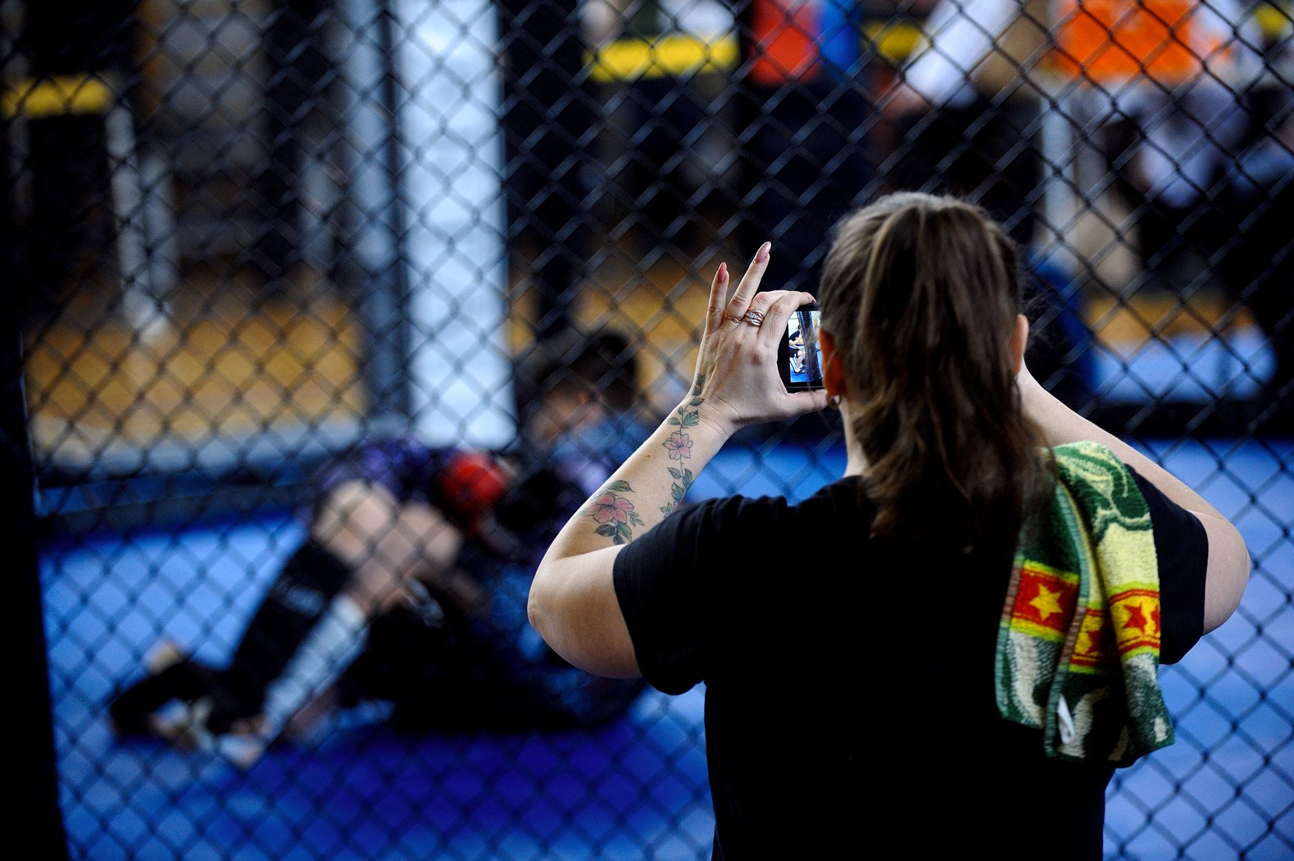 A woman records a mixed martial arts match using her smartphone inside the ring.