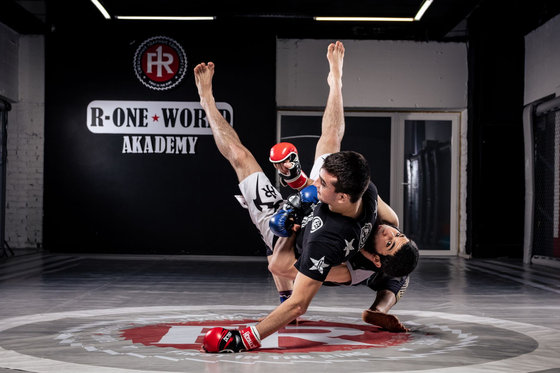 Two men engage in intense martial arts practice at an indoor academy gym.