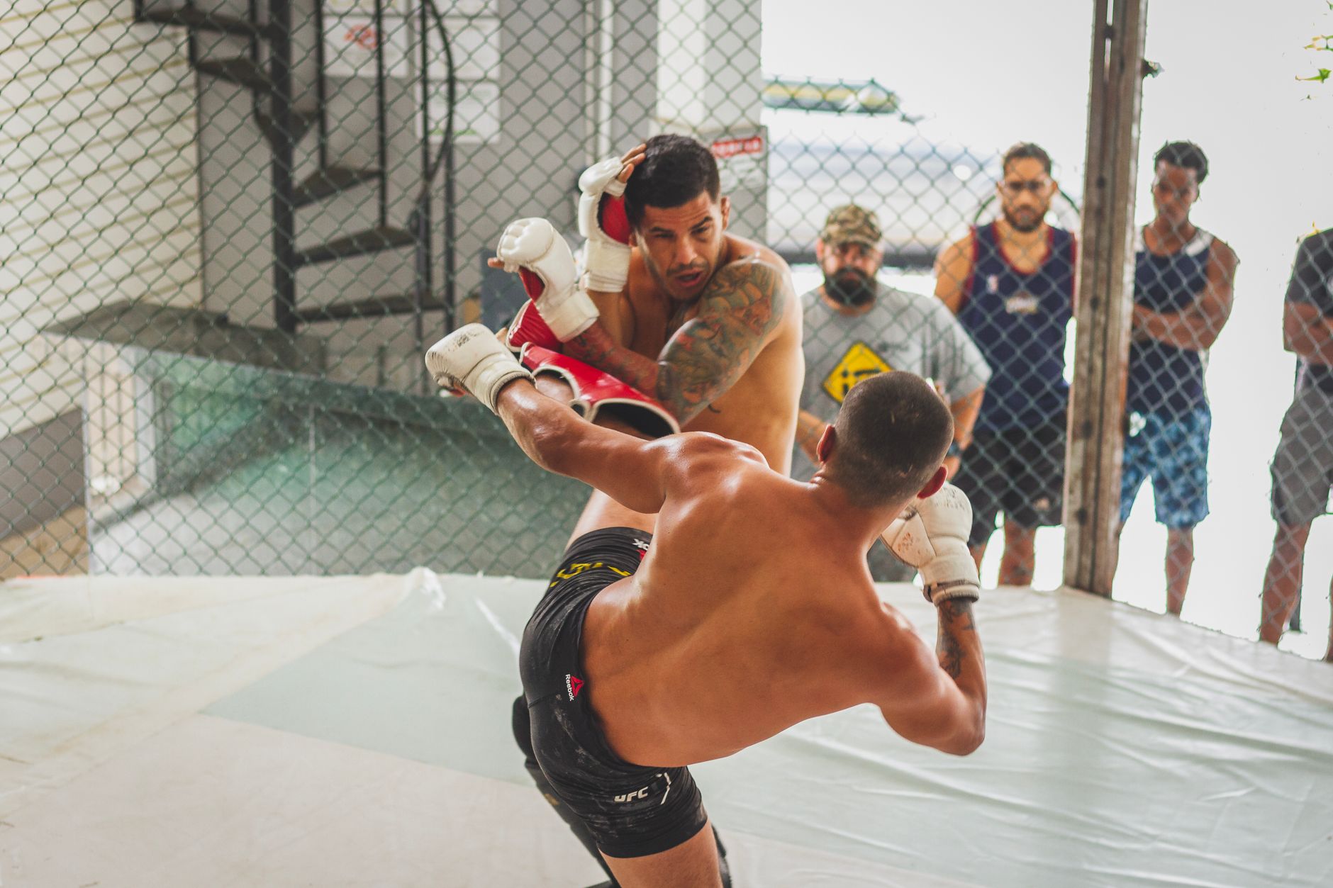 Two men sparring in a gym showcasing kickboxing skills with an audience watching.