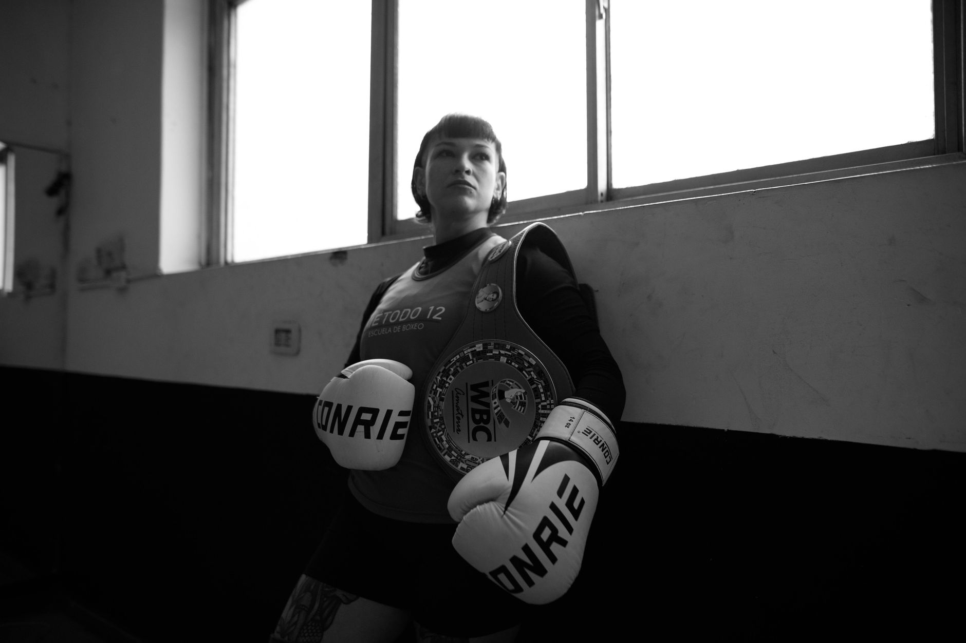 Black and white photo of a female boxer posed indoors with WBC title belt.