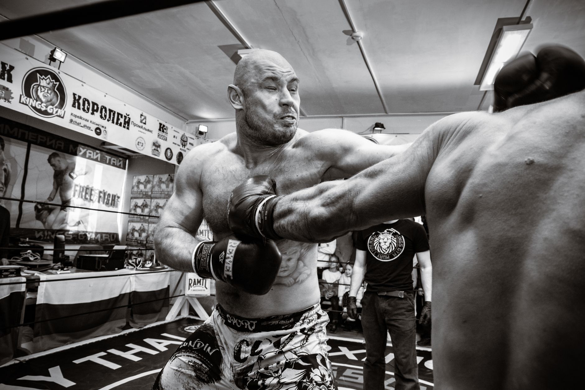 Grayscale image capturing intense action of MMA fighters in a gym setting with a punch in motion.