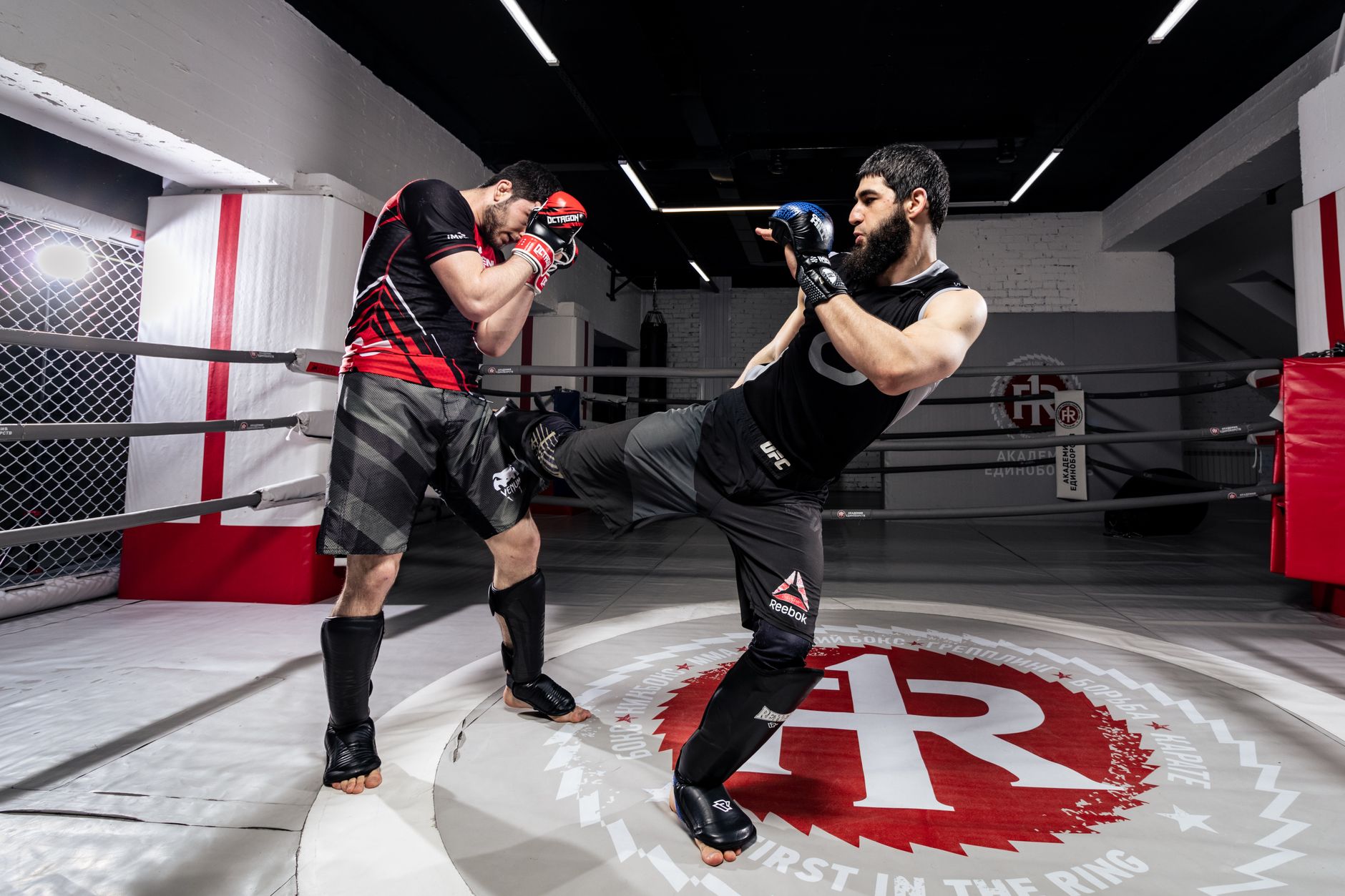 Two men practicing kickboxing in a gym, showcasing martial arts skills in a training ring.