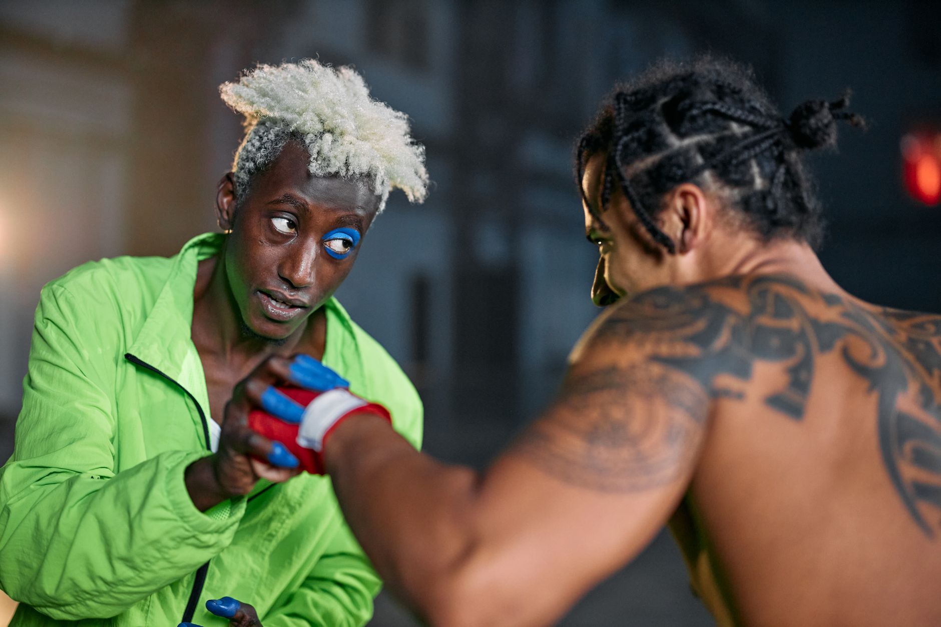 Two martial artists in an intense urban setting, displaying combat skills and tattoos.