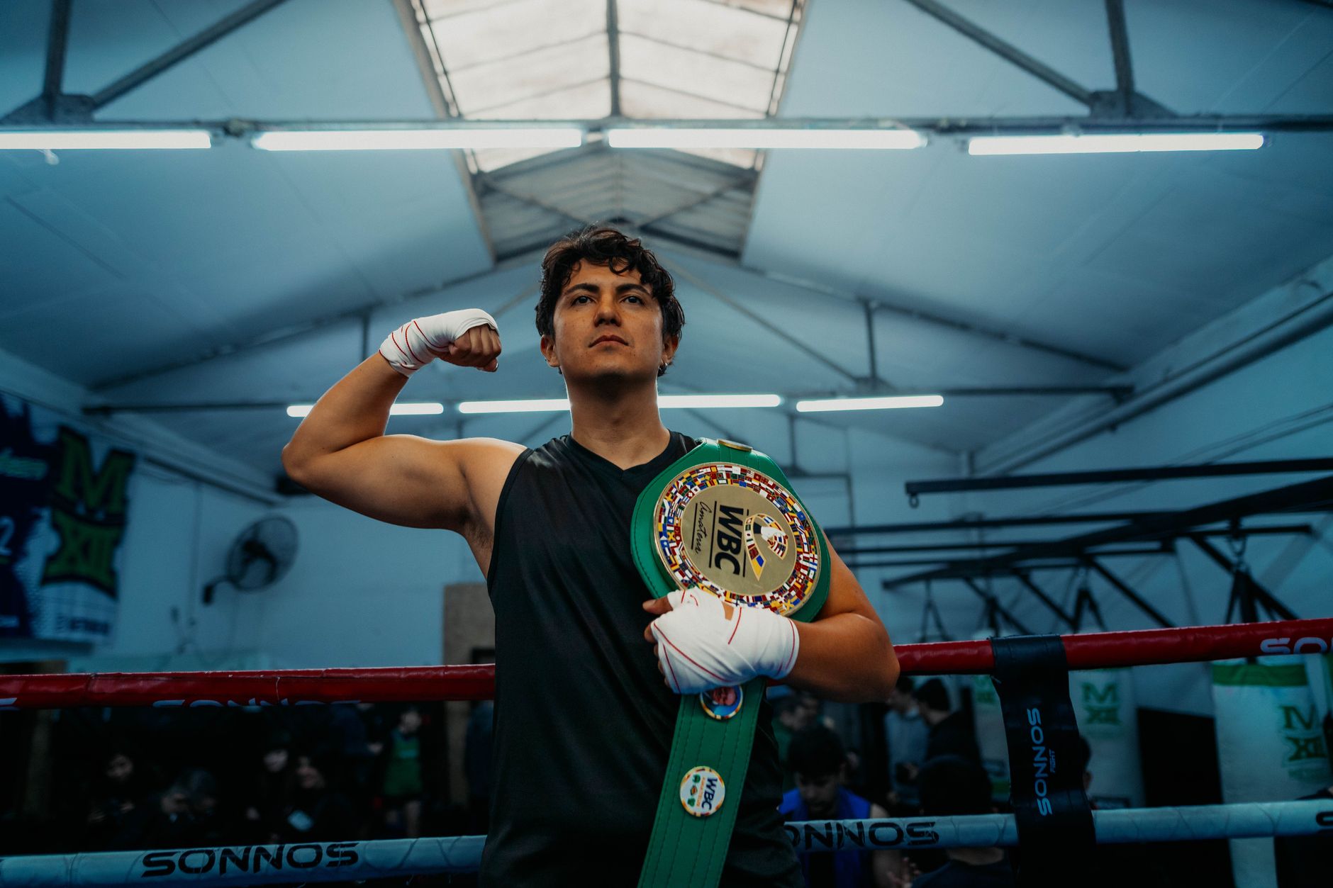 Boxer proudly holds a championship belt in an indoor gym setting.