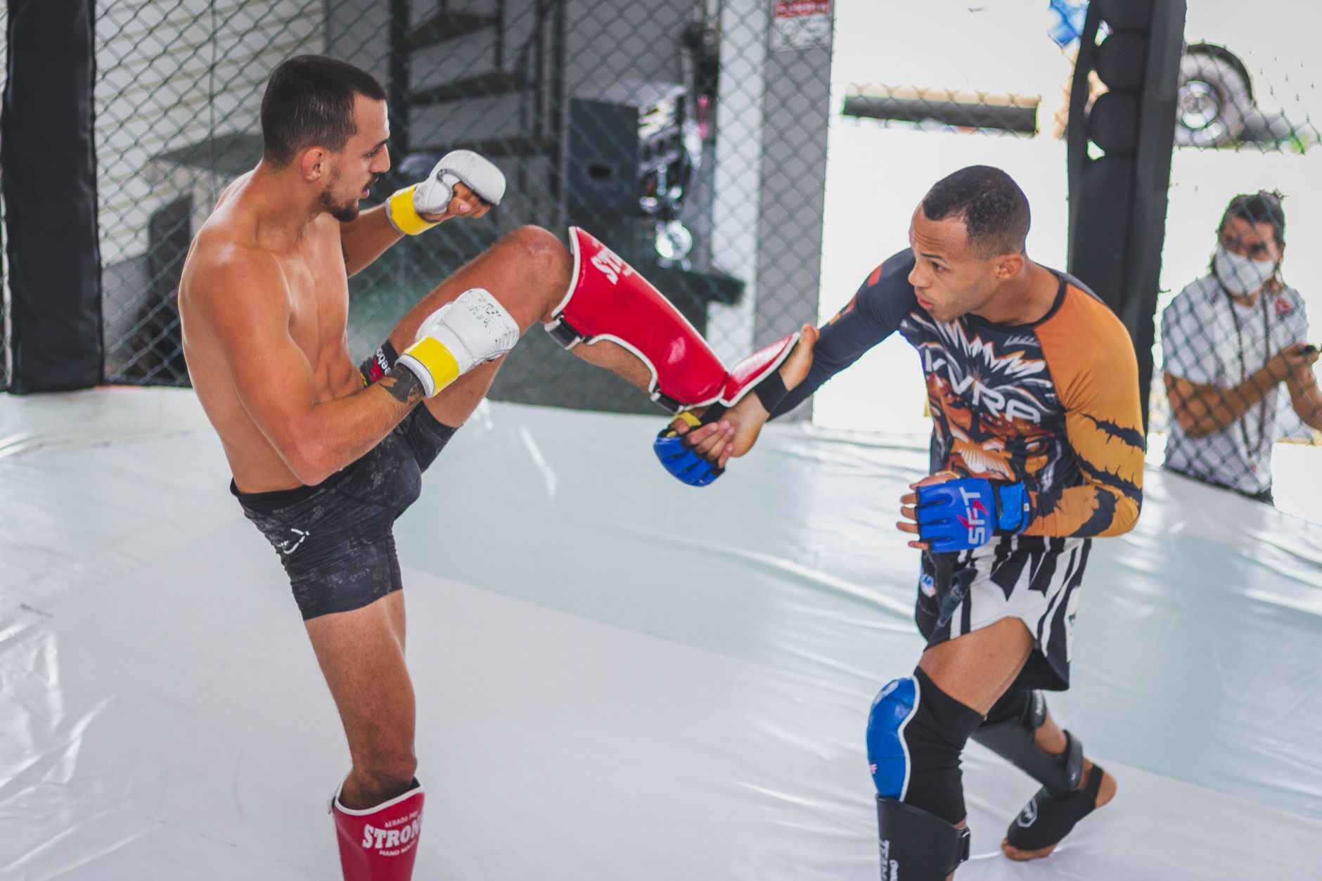 Two martial artists sparring in an indoor cage, showcasing dynamic fighting skills and athleticism.