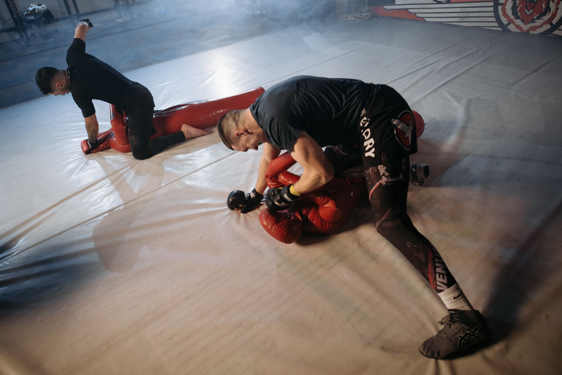 Two men practice MMA grappling moves indoors in a gym environment, focusing on skills and technique.