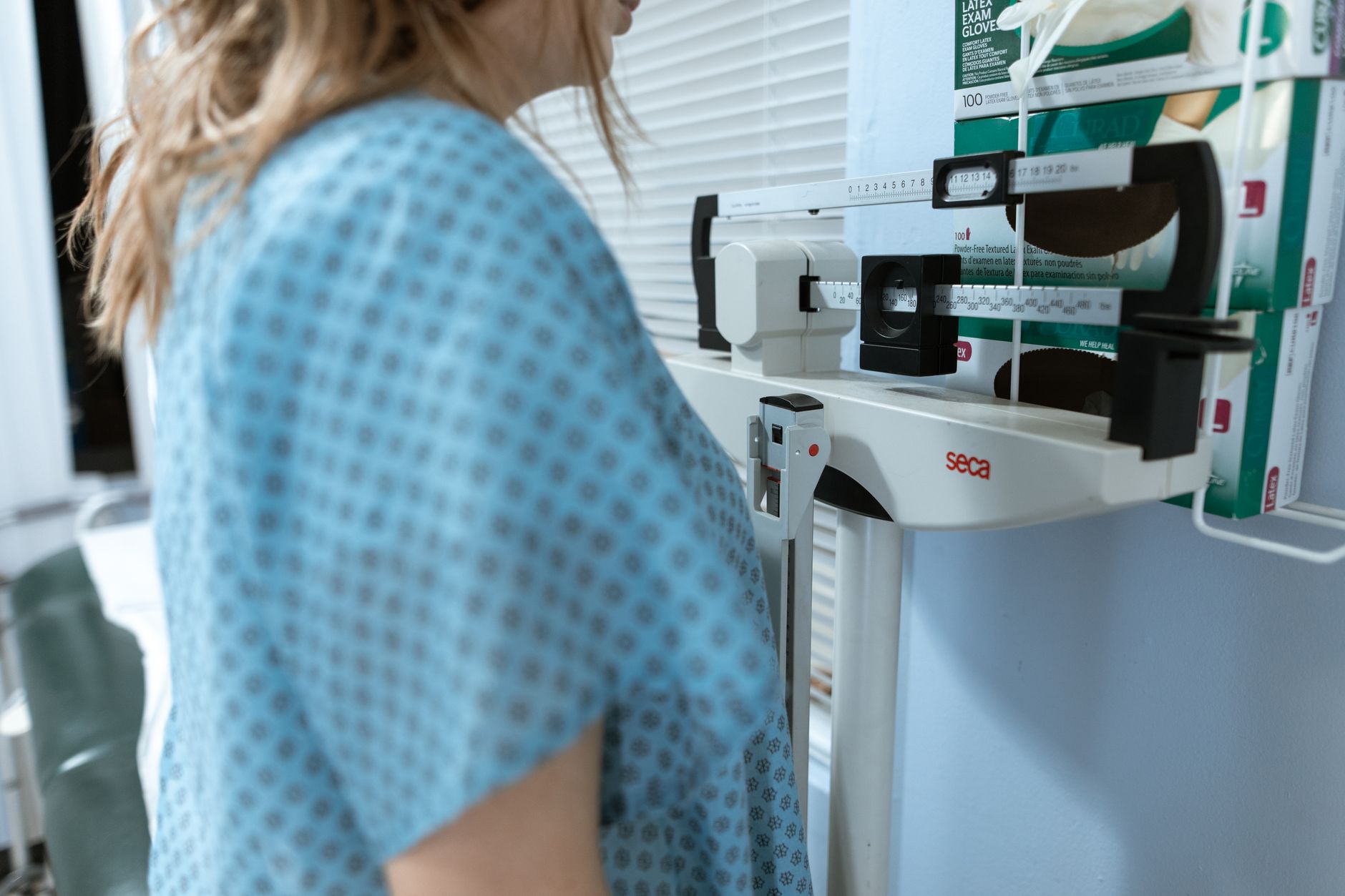 Adult female using a medical weighing scale in a healthcare setting.