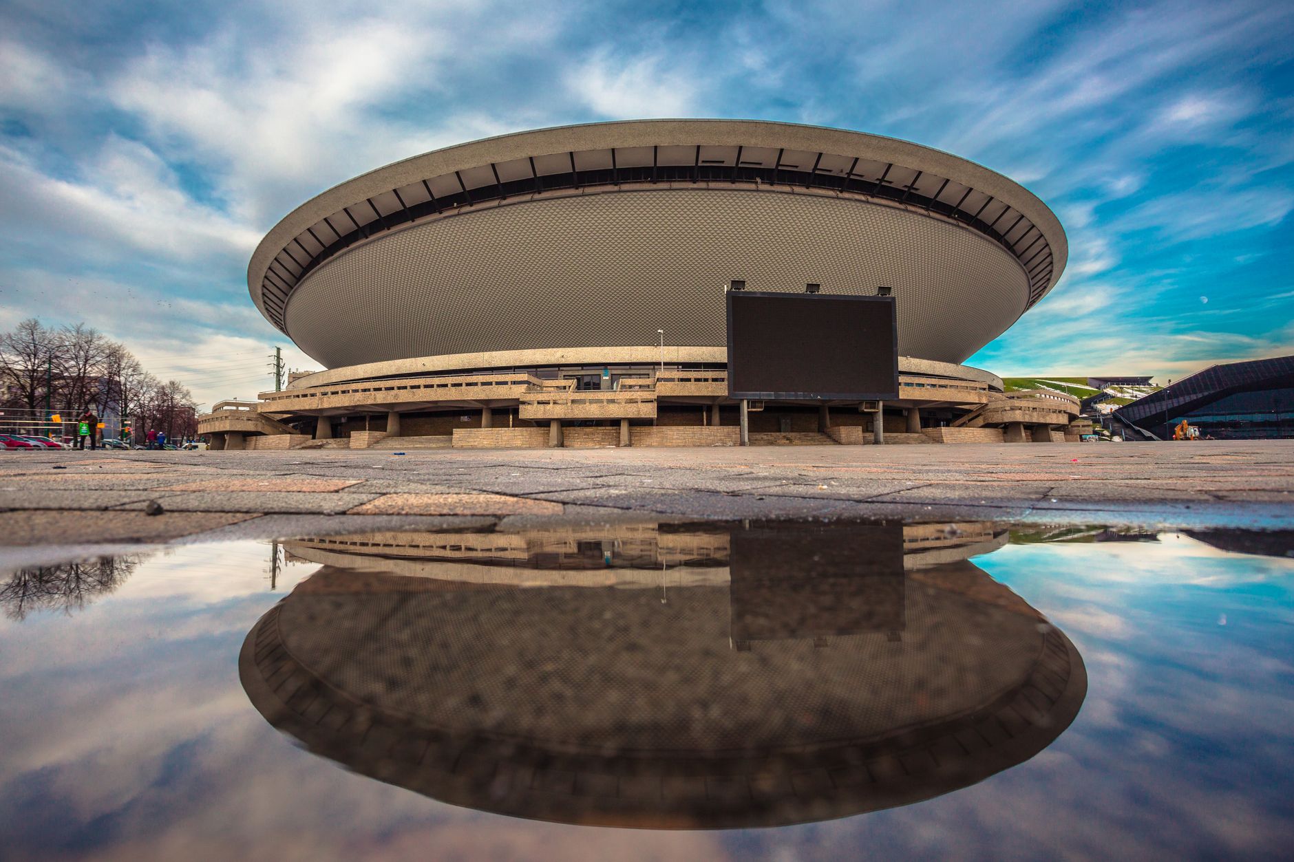 A stunning view of the Spodek Arena in Katowice, Poland, reflecting in a puddle.