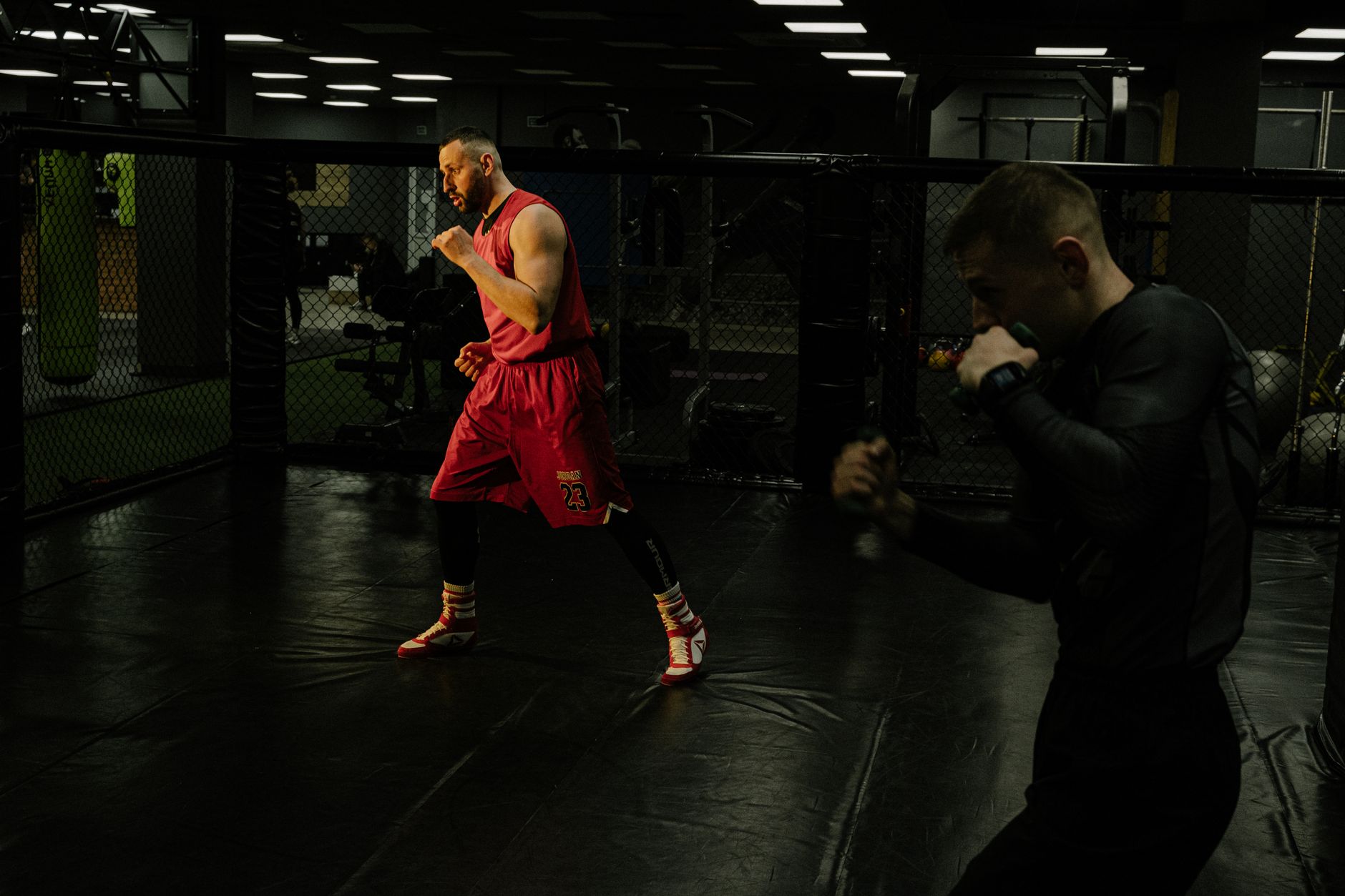 Two men practice boxing techniques in a dimly-lit gym, focusing on form and agility.