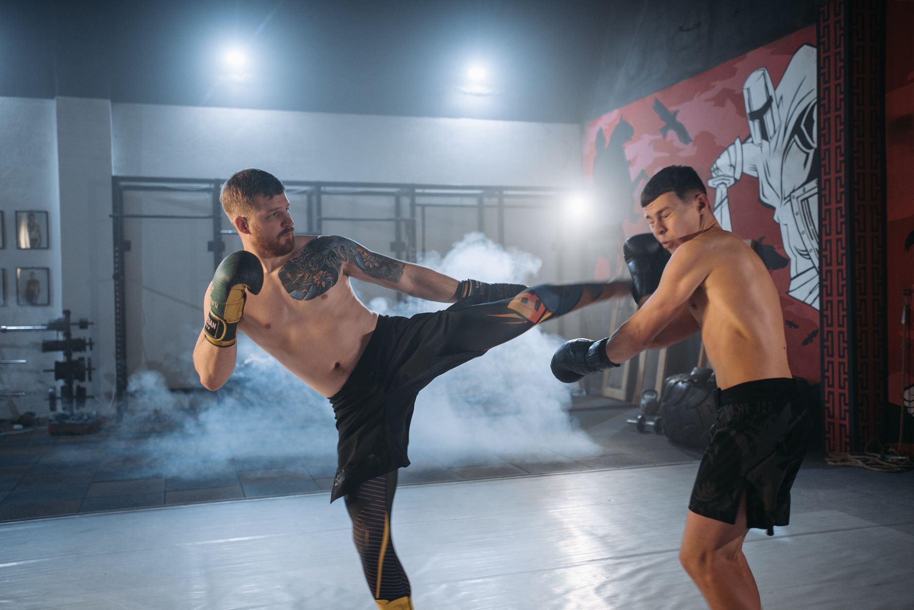 Two shirtless men engaging in vigorous MMA sparring, demonstrating skill and intensity indoors.