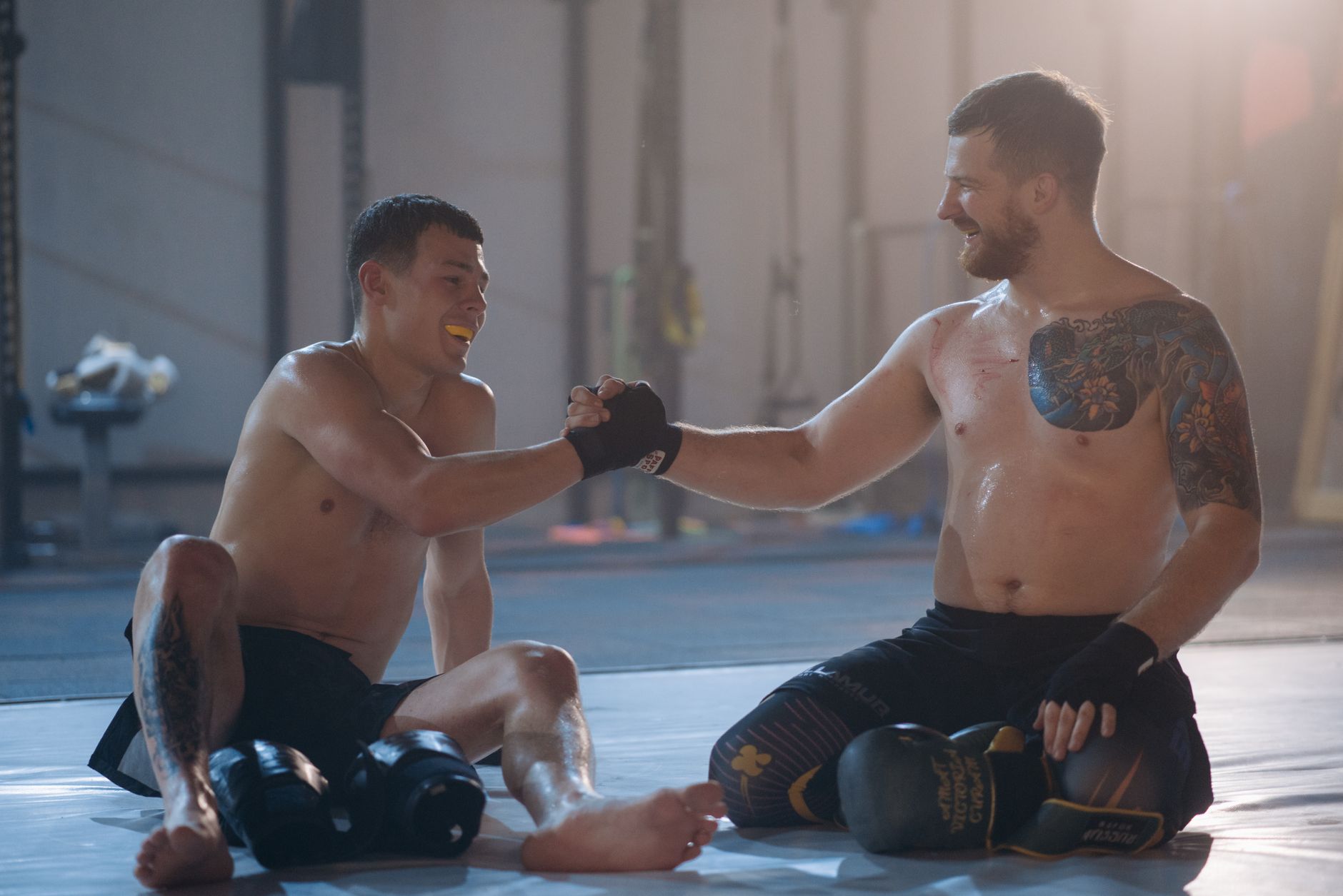 Two male martial artists sitting on the mat post-training, embracing sportsmanship with a handshake.