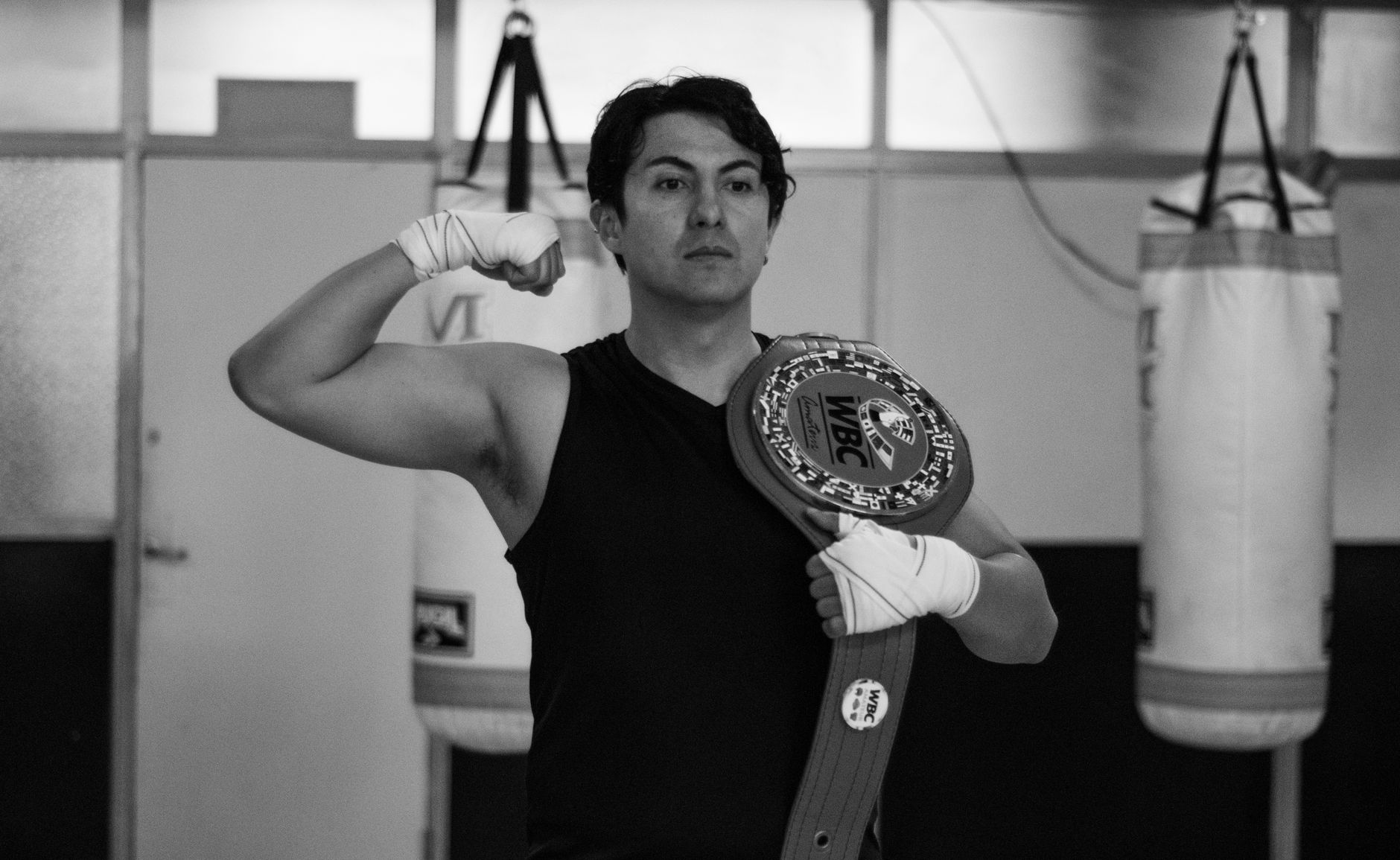A strong boxer in a gym poses with a championship belt, showcasing strength and victory.