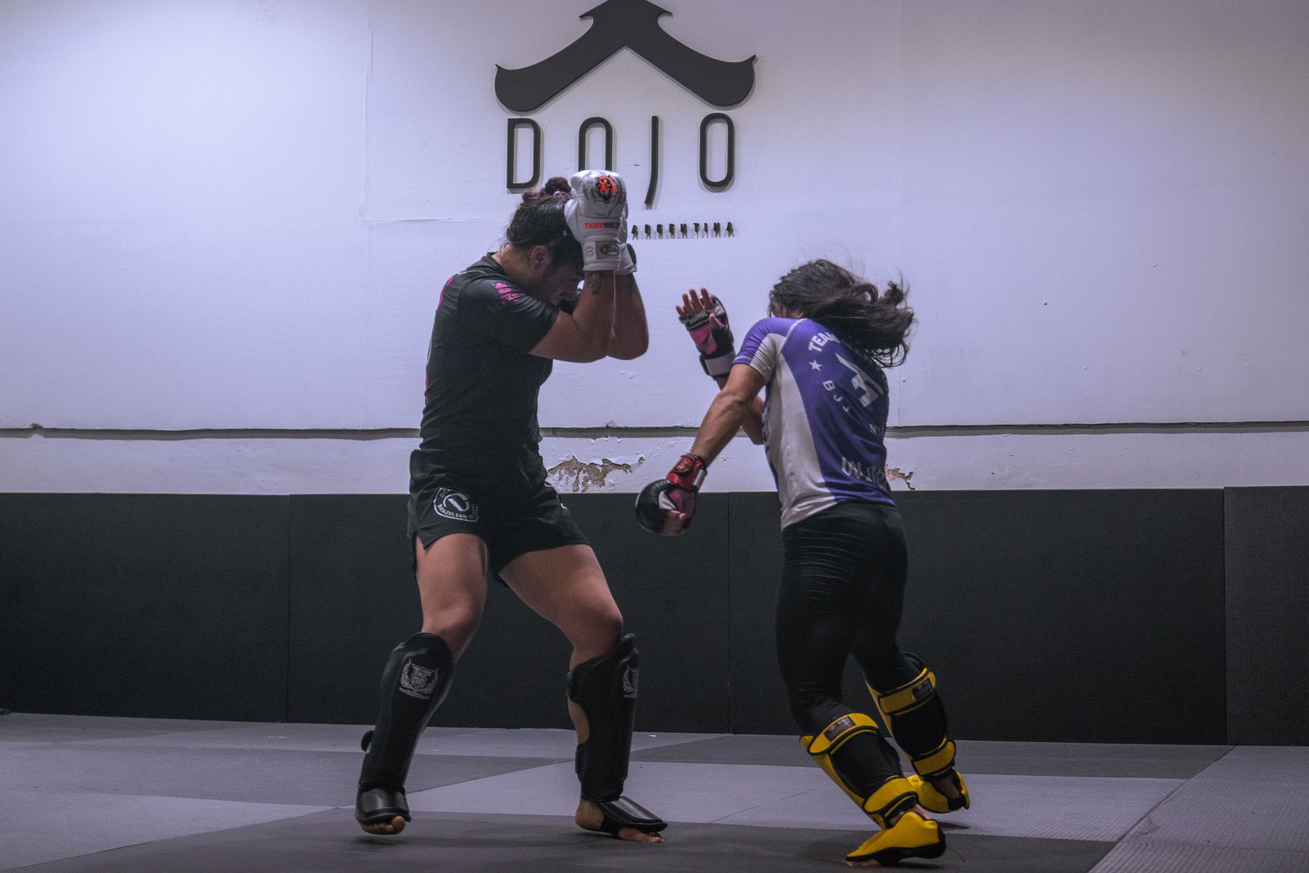 Two female athletes engage in a rigorous sparring session in a martial arts dojo.