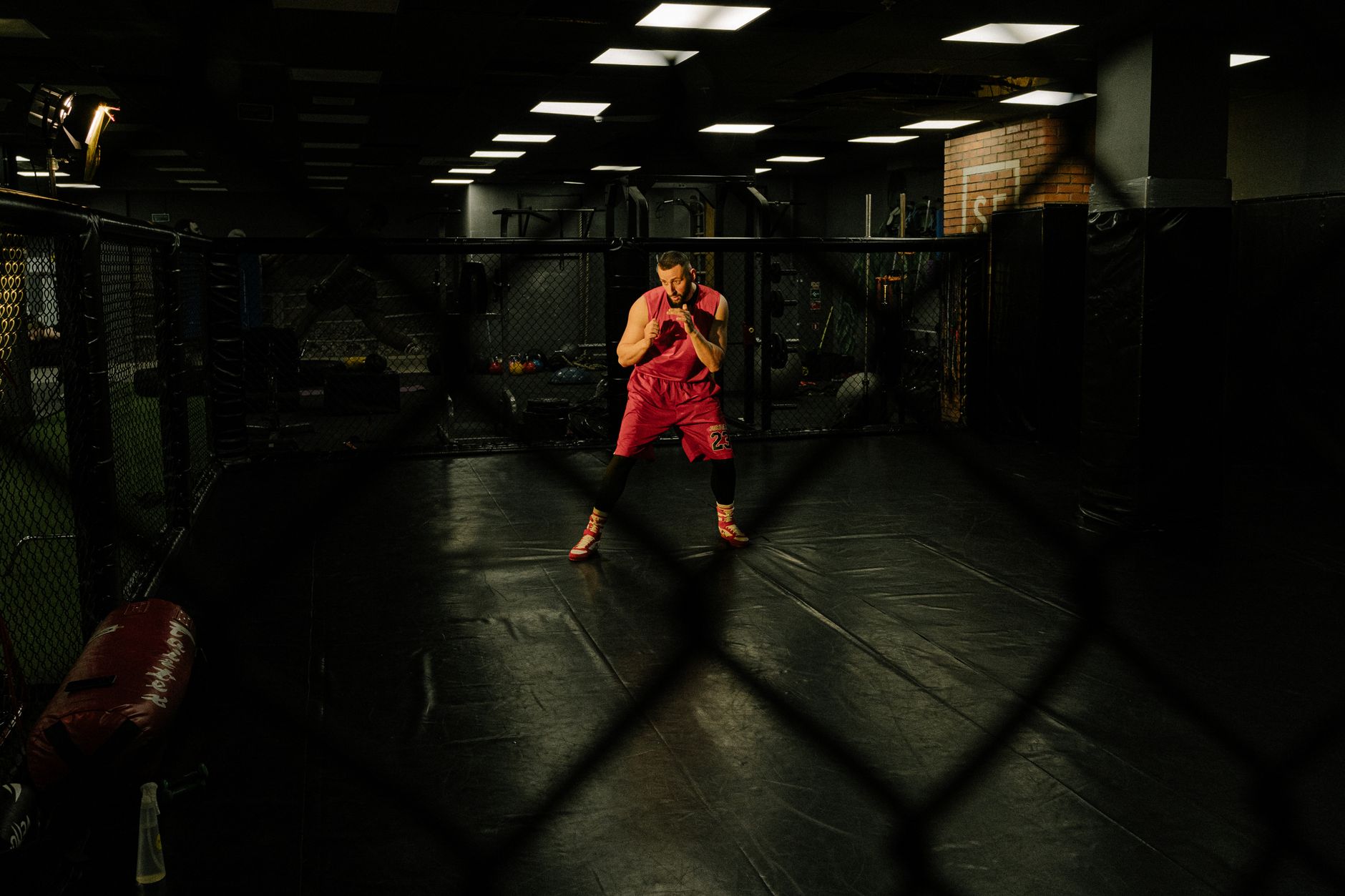 Male athlete wearing red activewear training intensely in an indoor martial arts gym. Dark and focused setting.
