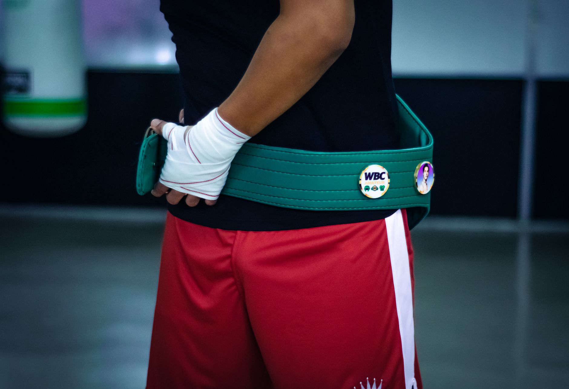 Close-up of a boxer wearing a championship belt in a gym setting, showcasing preparation and focus.