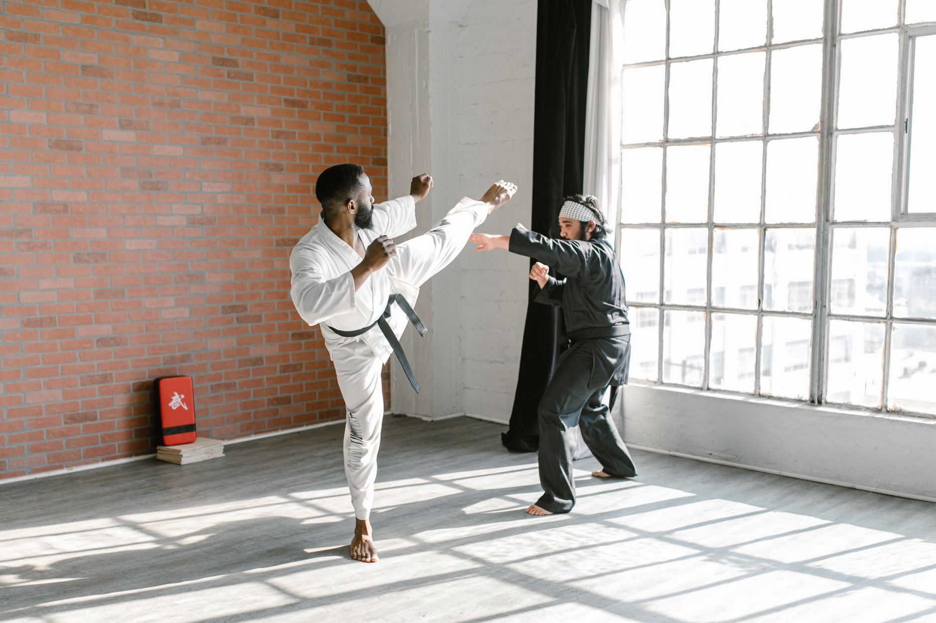 Two martial artists sparring in a sunlit dojo, showcasing discipline and skill.