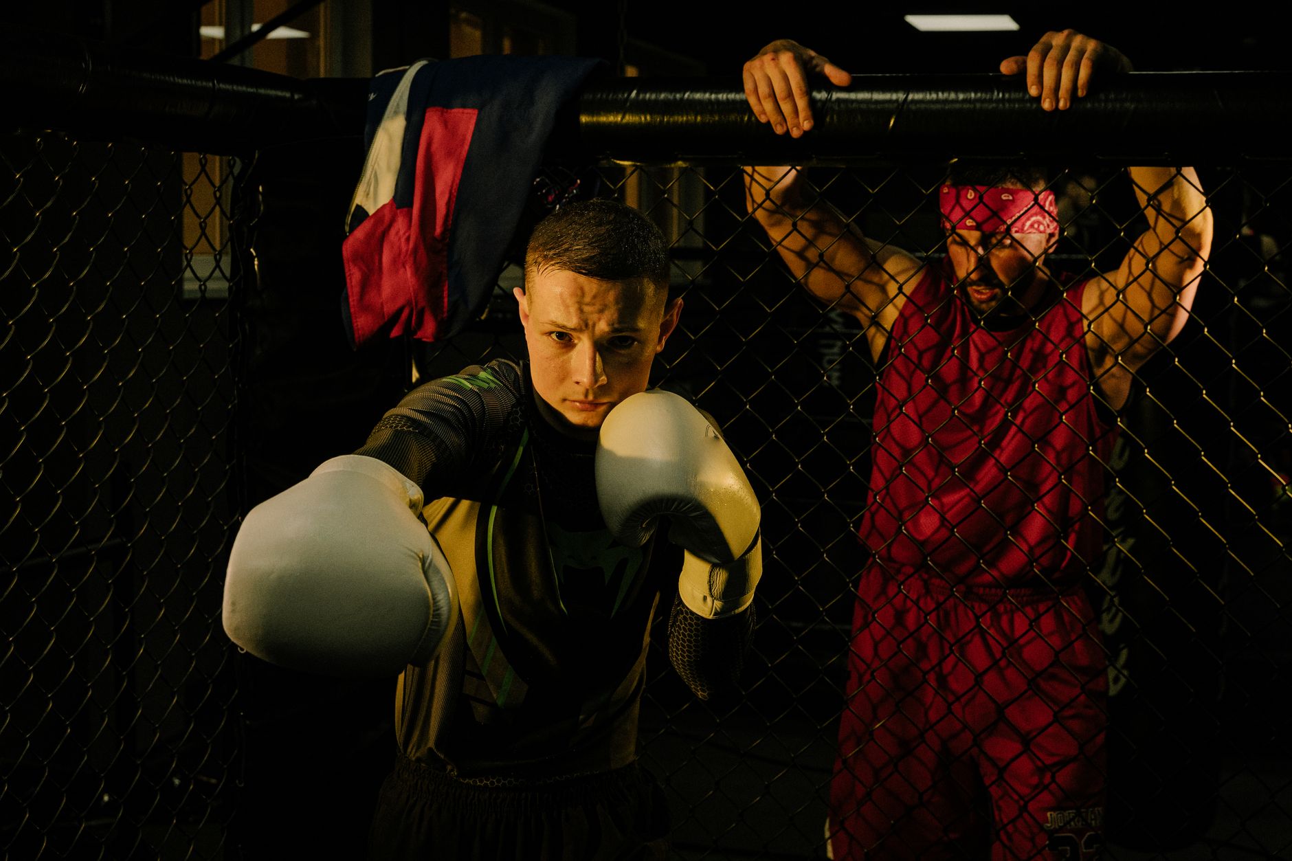Boxer in white gloves sparring with trainer in a cage fighting ring, martial arts focus.