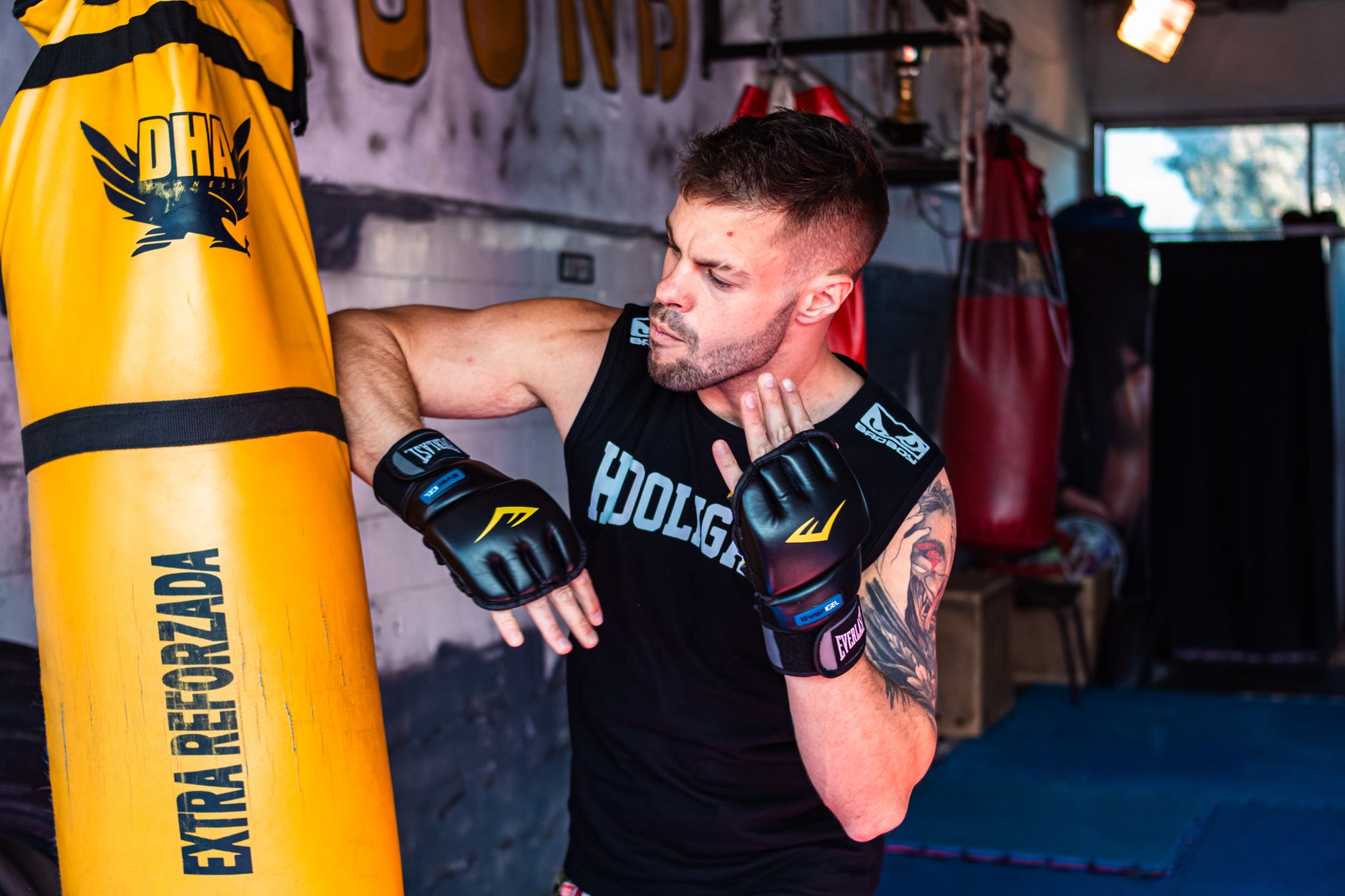 A focused fighter practicing martial arts striking a punching bag in a gym setting.