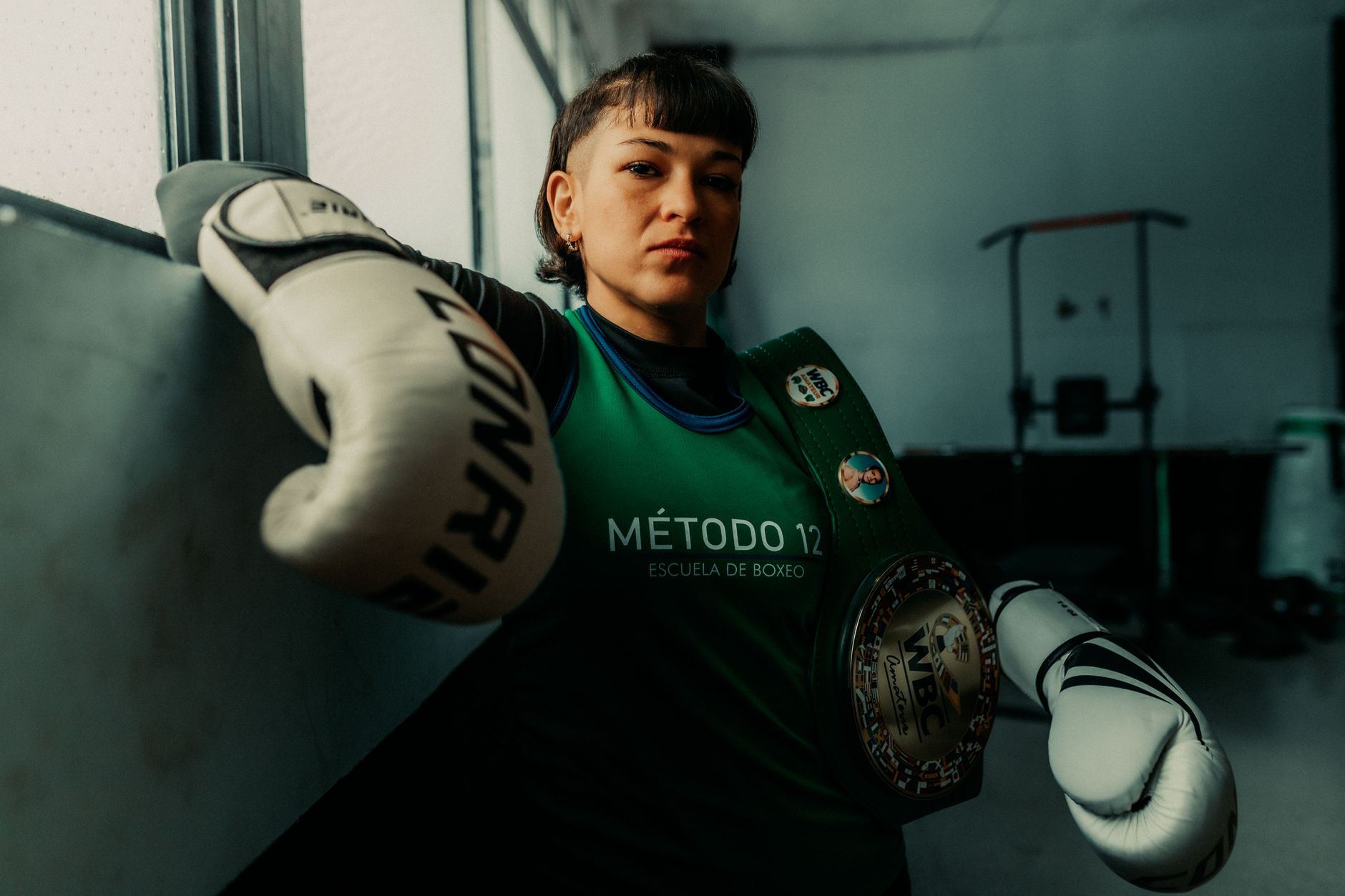 Female boxer in an Argentine gym with championship belt, exuding confidence and strength.