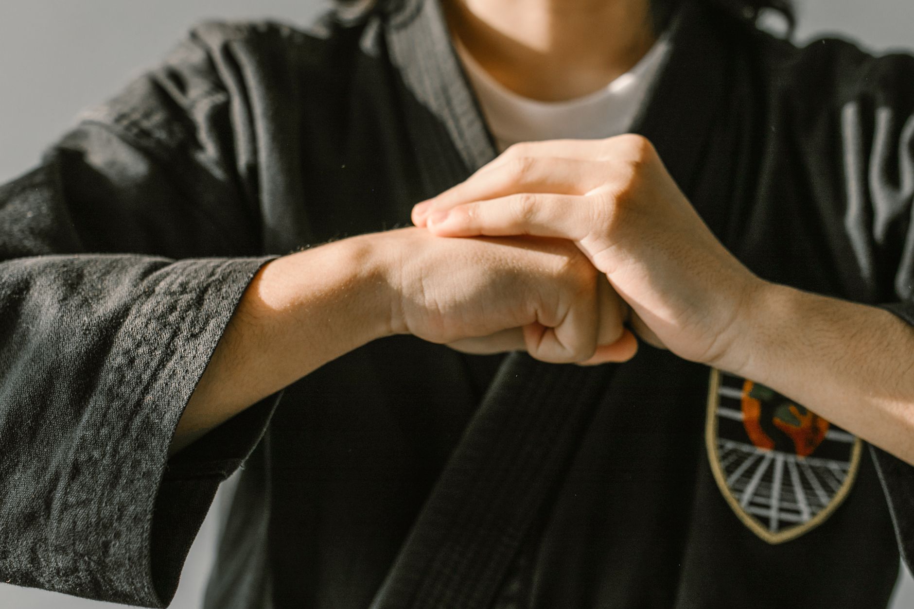 Close-up of a martial artist in a black gi performing a traditional fist gesture.