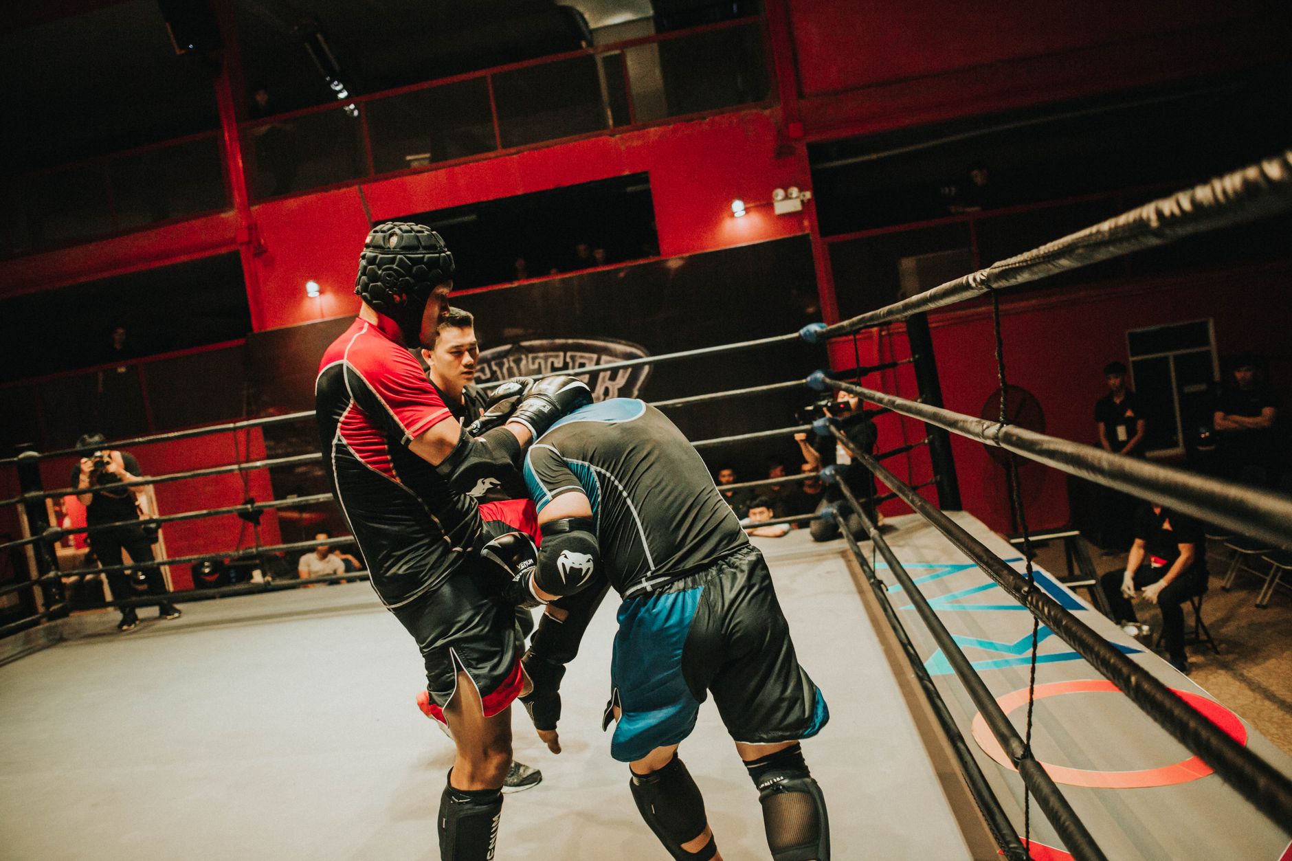 Two athletes compete in a fierce boxing match inside a well-lit indoor arena.