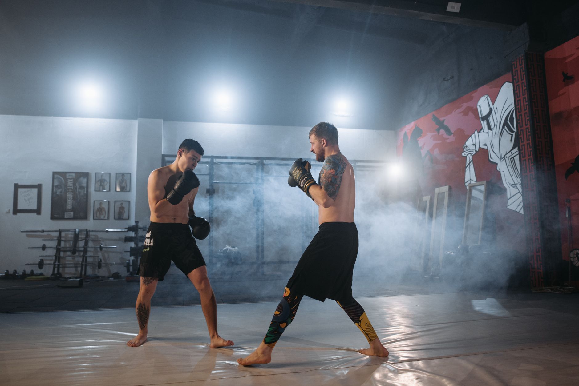 Two male fighters sparring in an indoor gym with mist and dramatic lighting.