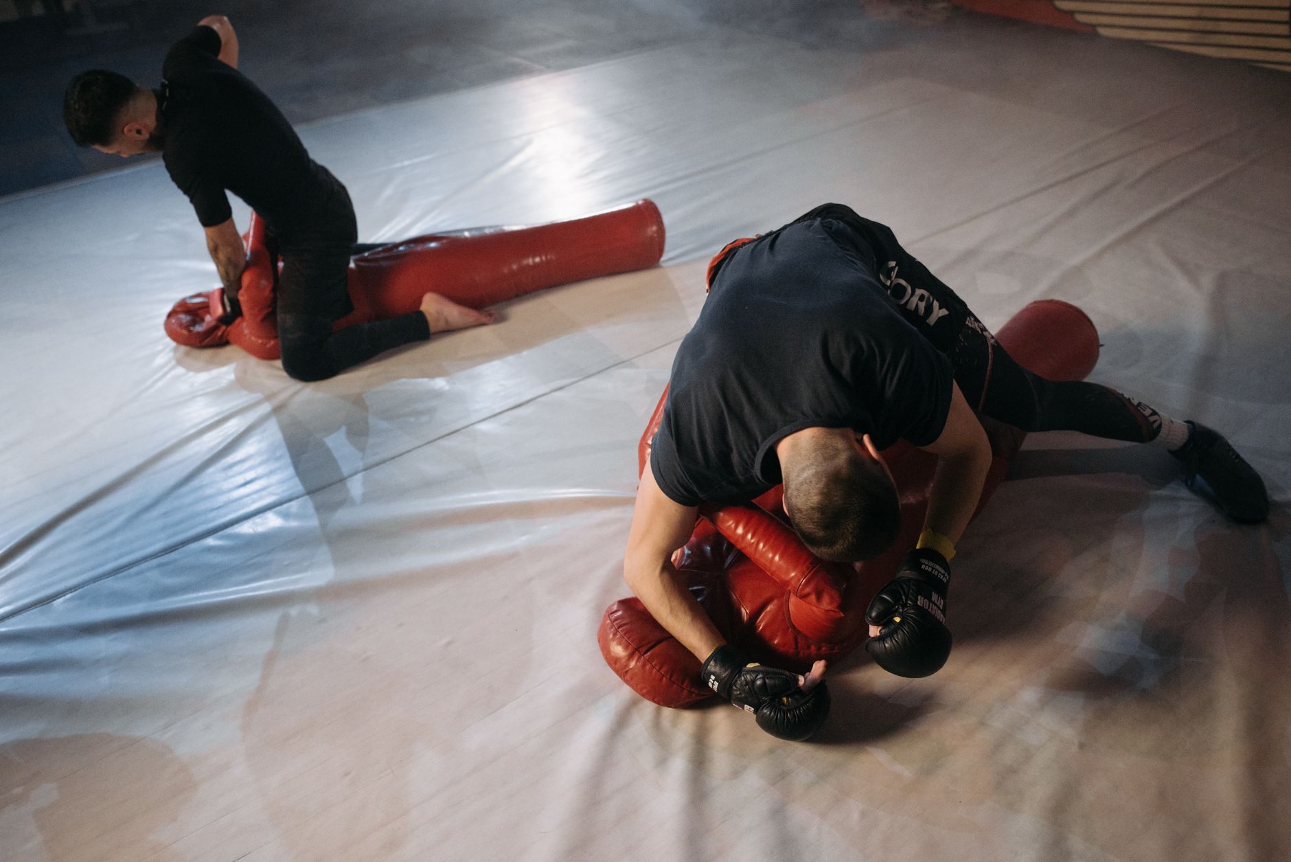 Two mixed martial arts fighters training with grappling dummies in a gym setting.