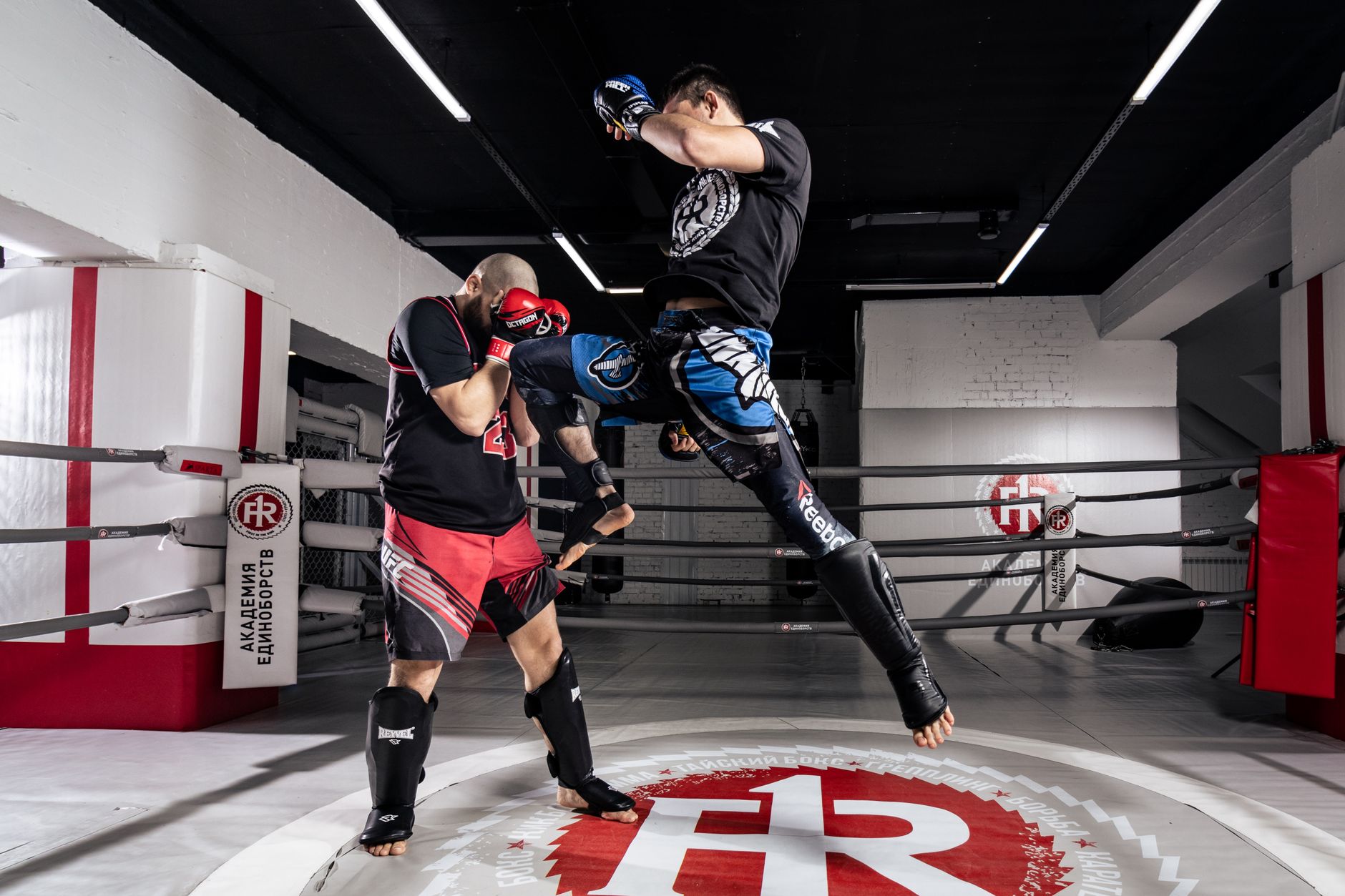 Two men engaged in intense kickboxing training inside a professional ring.