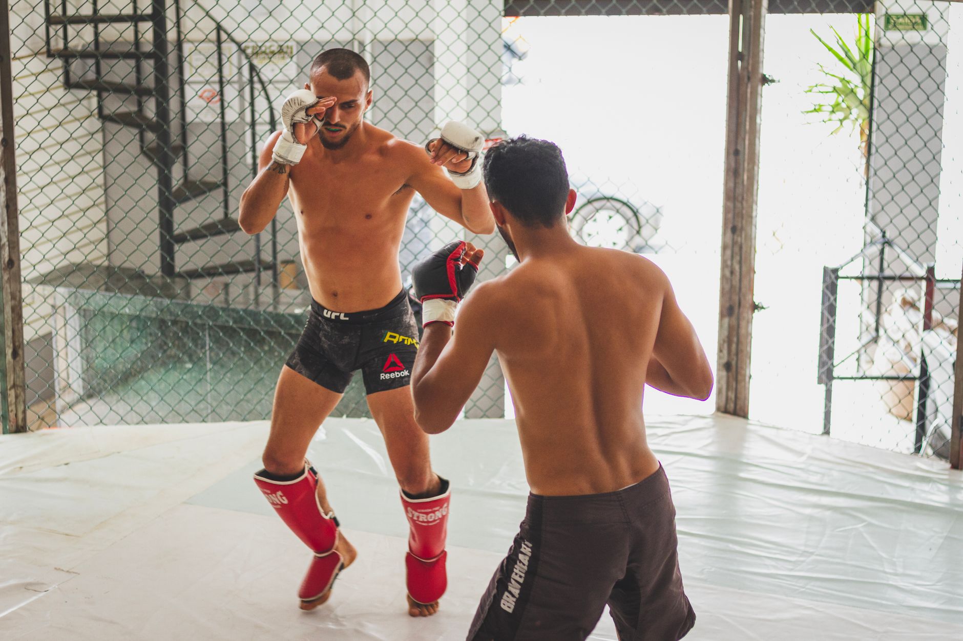 Two men practicing mixed martial arts sparring in a gym's cage.