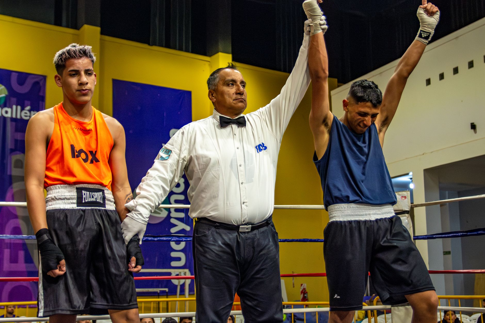 A referee declares the winner of a boxing match as one boxer's arm is raised in triumph.