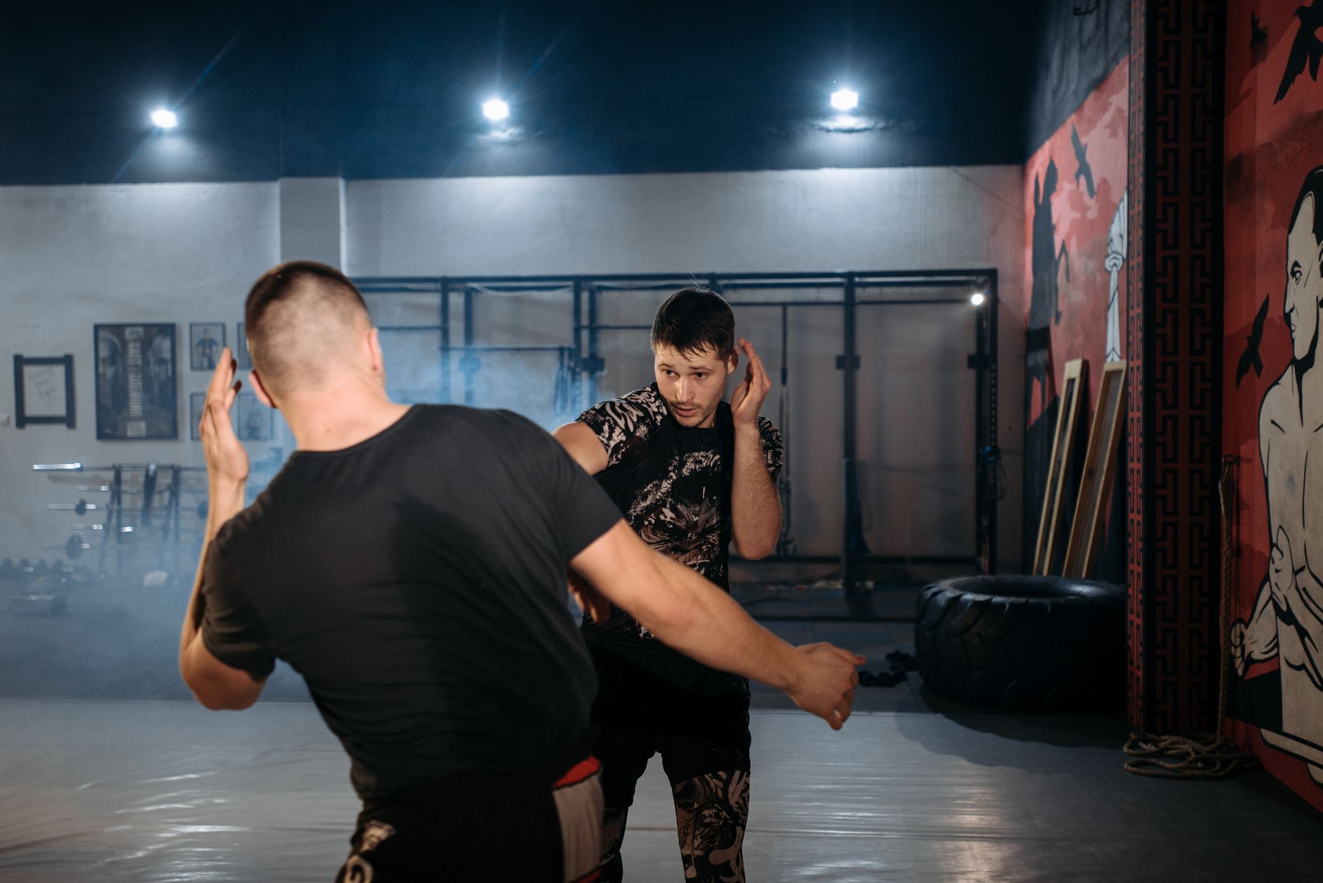 Two men engage in a dynamic martial arts sparring session at an indoor gym.