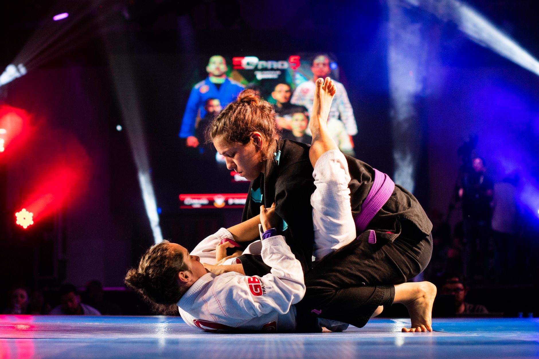 Women compete in a dynamic Brazilian Jiu-Jitsu match on stage.