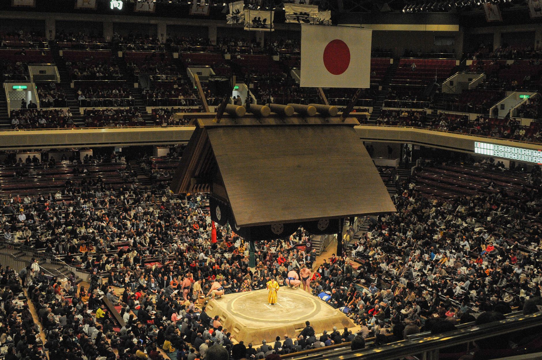 Large crowd watches a traditional sumo wrestling match inside a Japanese arena.