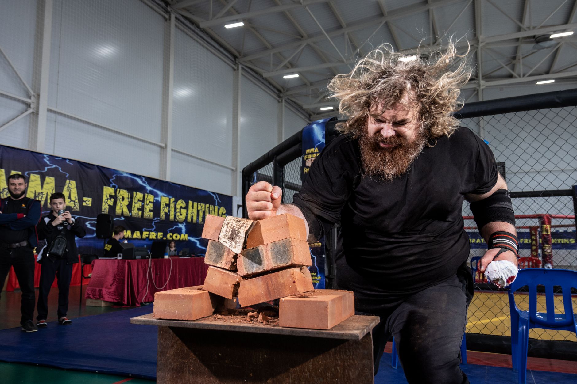 A strong man demonstrates brick breaking skills in an indoor MMA competition setting.